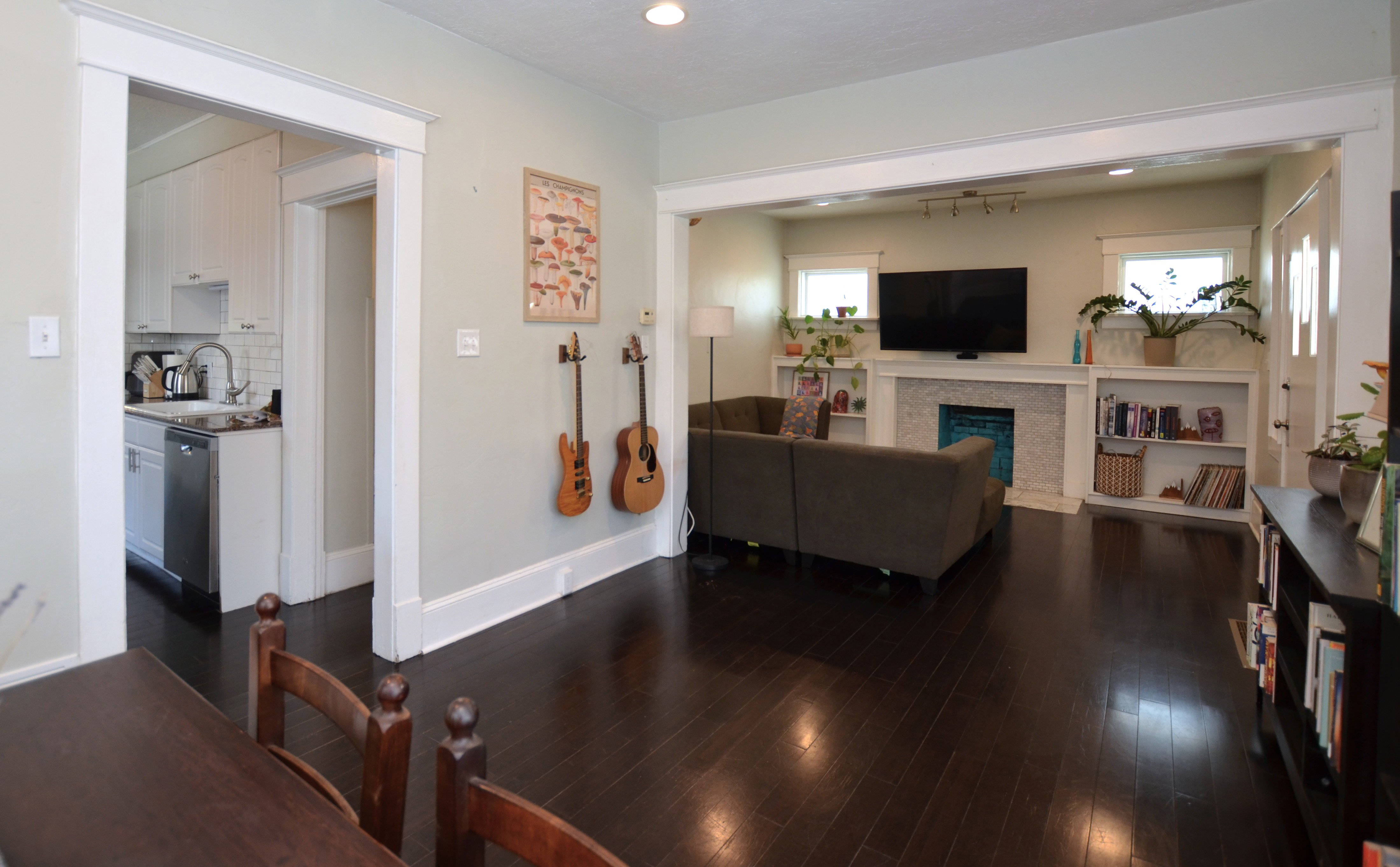 Hardwood-style flooring throughout, showcasing a fireplace with a decorative tile surround, built-in shelving, and a bright kitchen with white cabinetry and stainless steel appliances