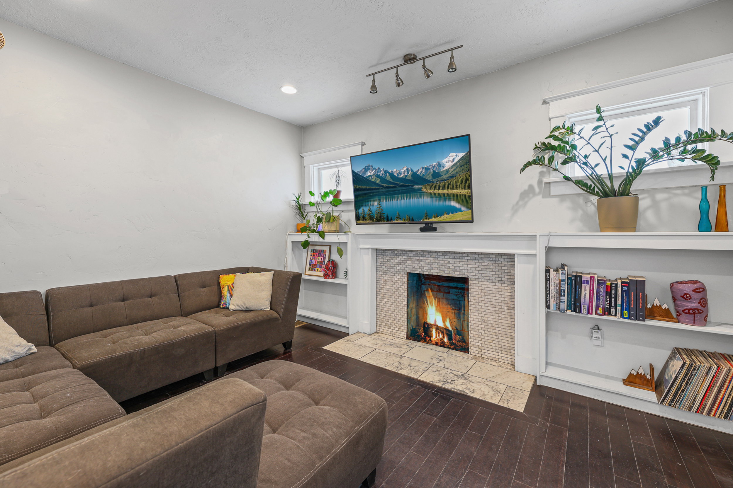Living area featuring a fireplace with a mosaic tile surround and stone hearth, dark wood-finish flooring, recessed lighting, track lighting, and built-in shelving