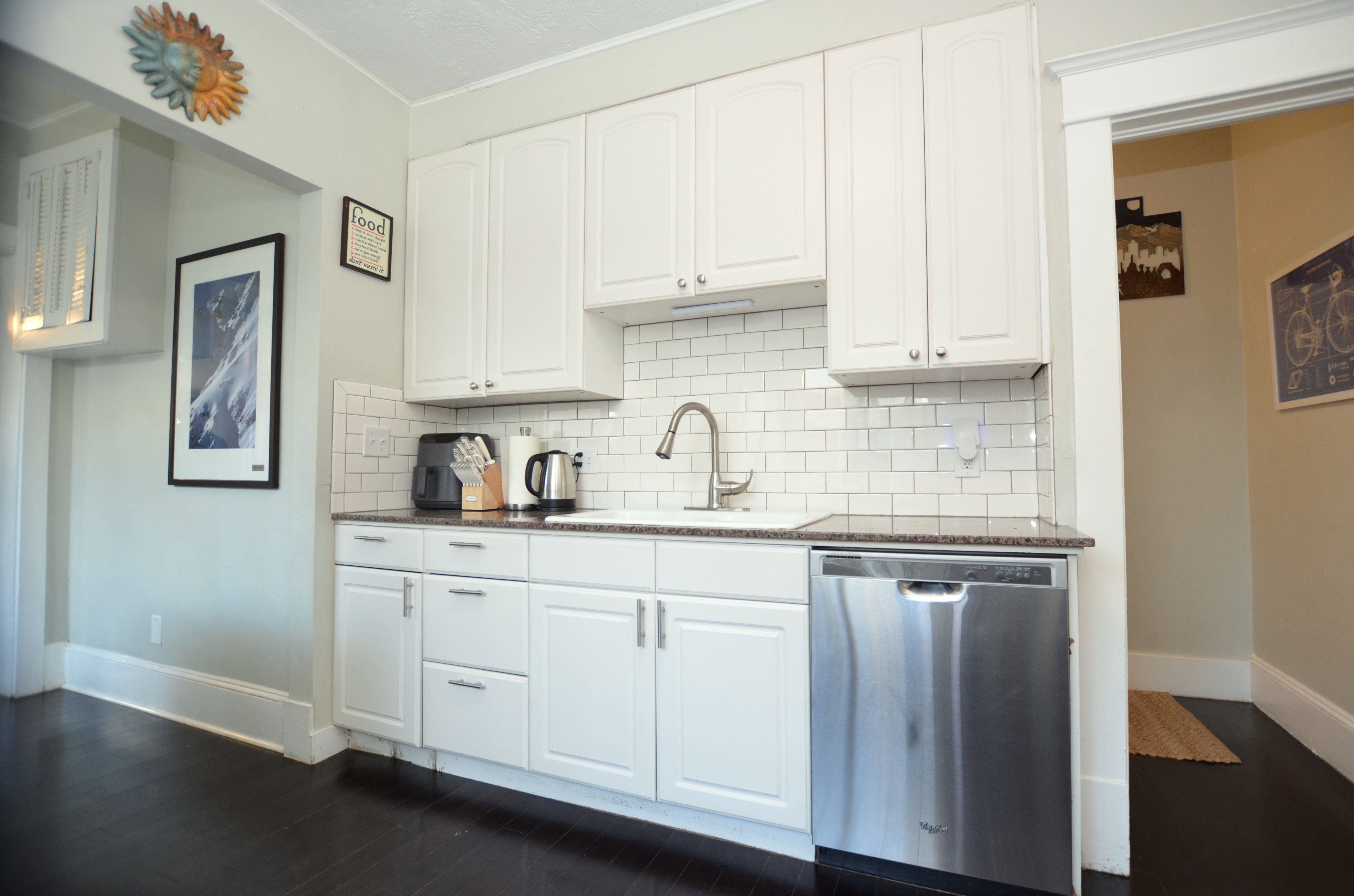 Kitchen featuring white cabinetry, subway tile backsplash, dark granite-style countertops, stainless steel Whirlpool dishwasher, and dark wood-finish flooring