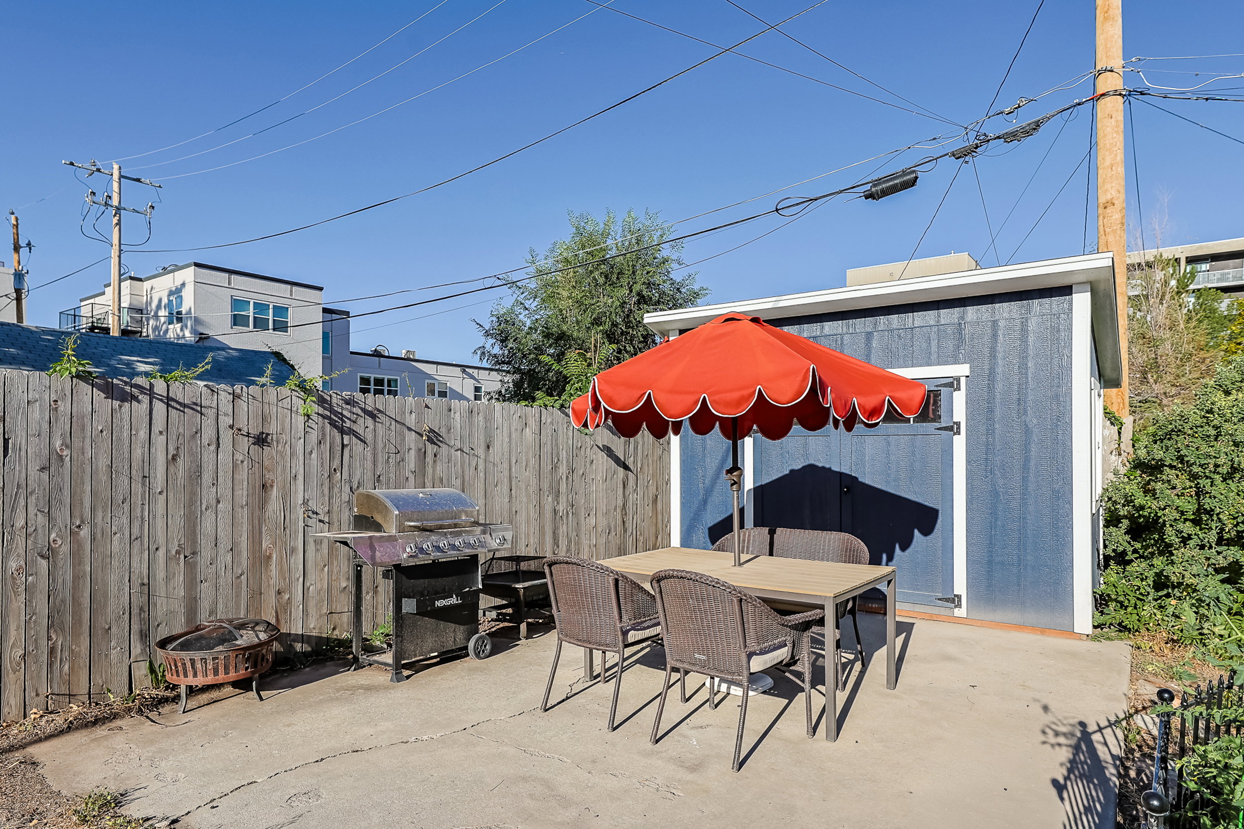 Outdoor patio area featuring a concrete surface, a wooden privacy fence, and a freestanding blue storage shed with white trim