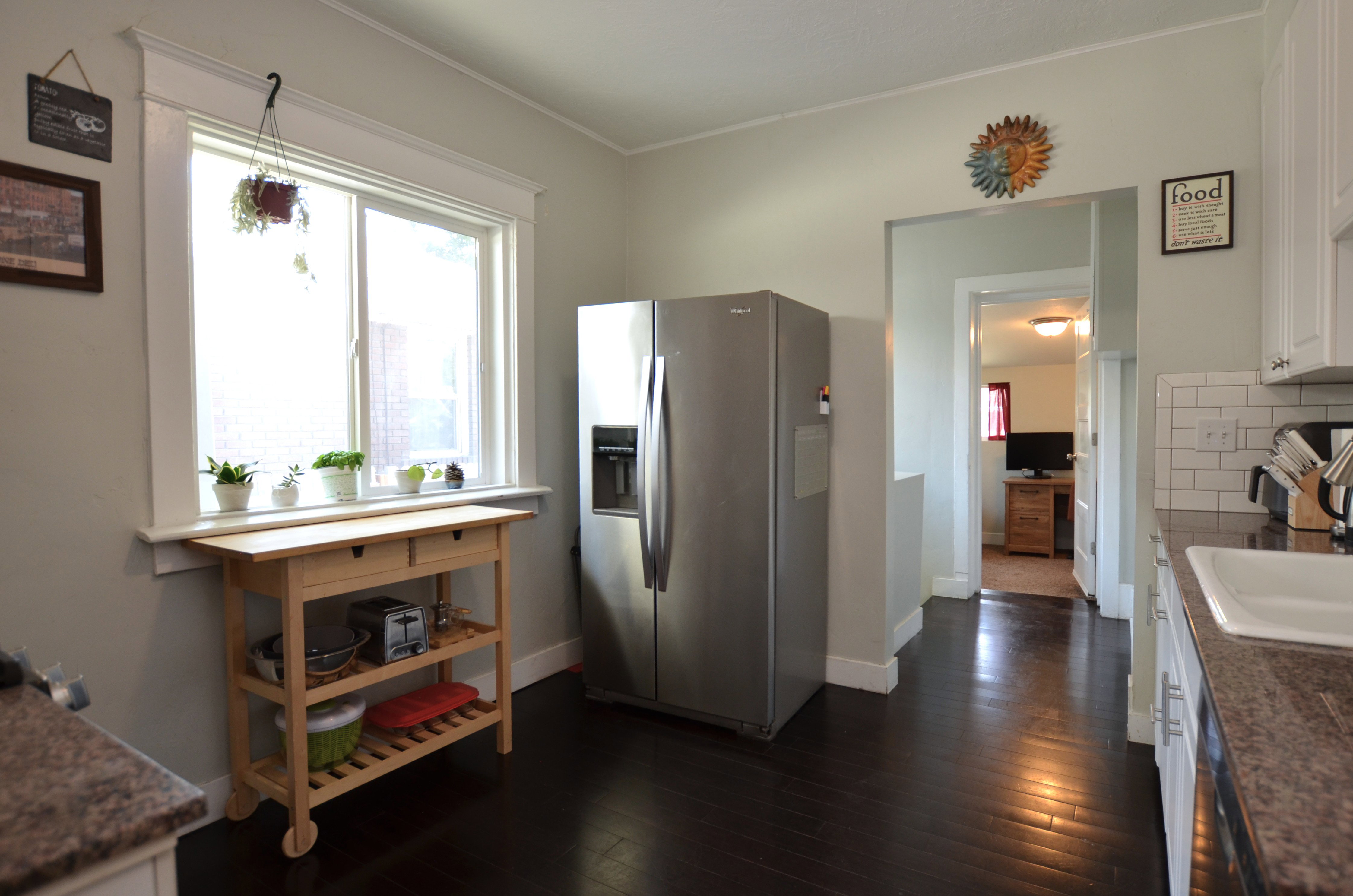 Spacious kitchen featuring dark wood-finish flooring, white cabinetry with silver-tone hardware, and a window with white trim