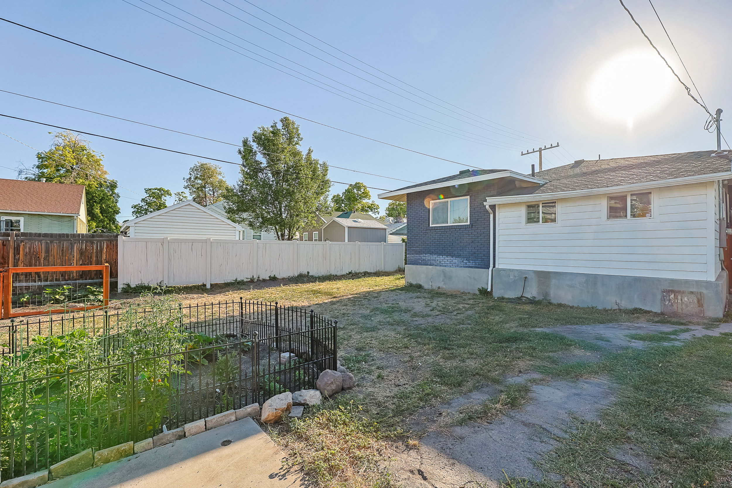Exterior rear of the property featuring a white vinyl fence, a partial wood fence, and a dedicated garden area with a black metal fence