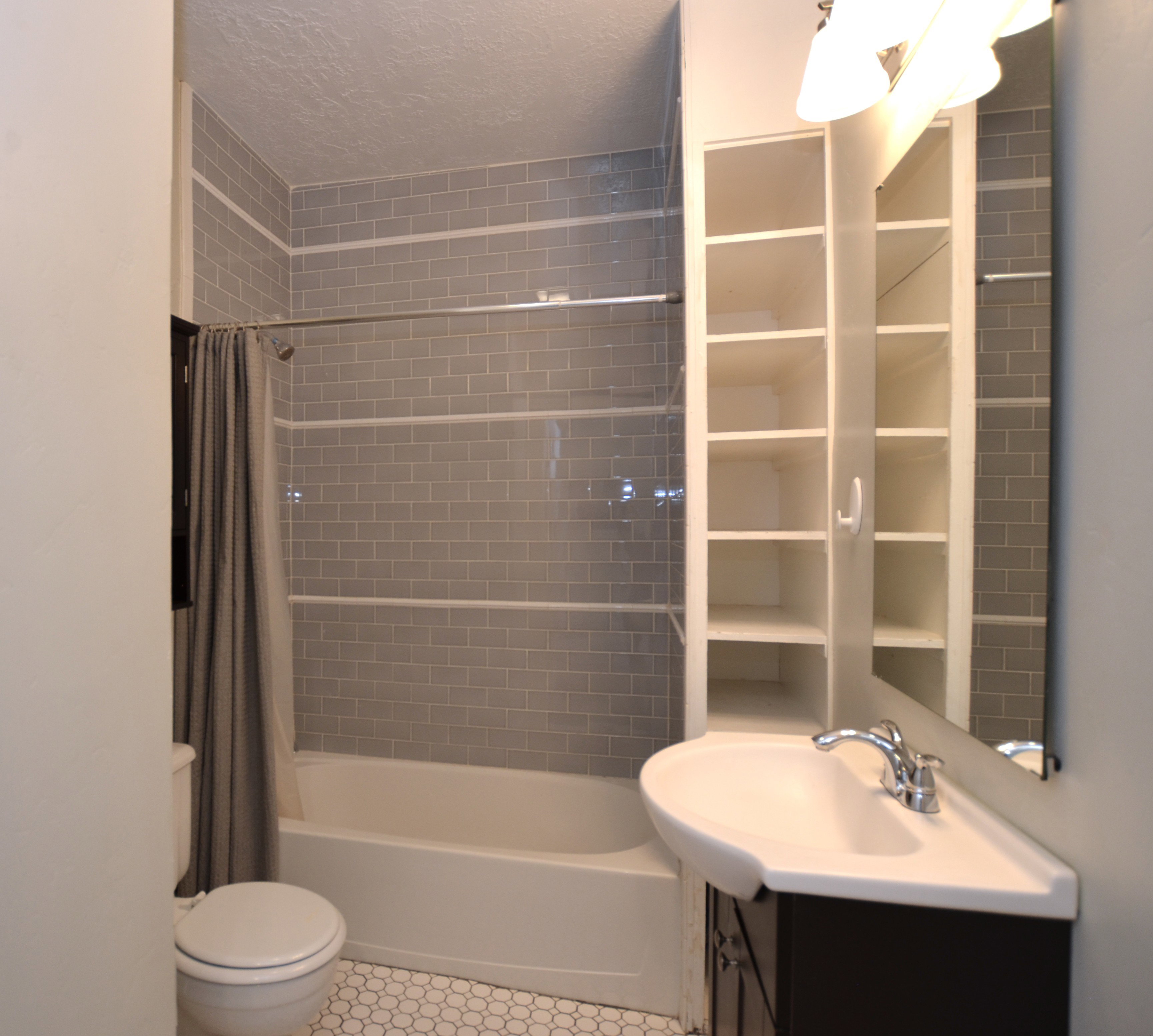 Bathroom featuring a bathtub with subway tile surround, white hexagonal floor tiles, a pedestal sink with chrome faucet, and built-in shelving