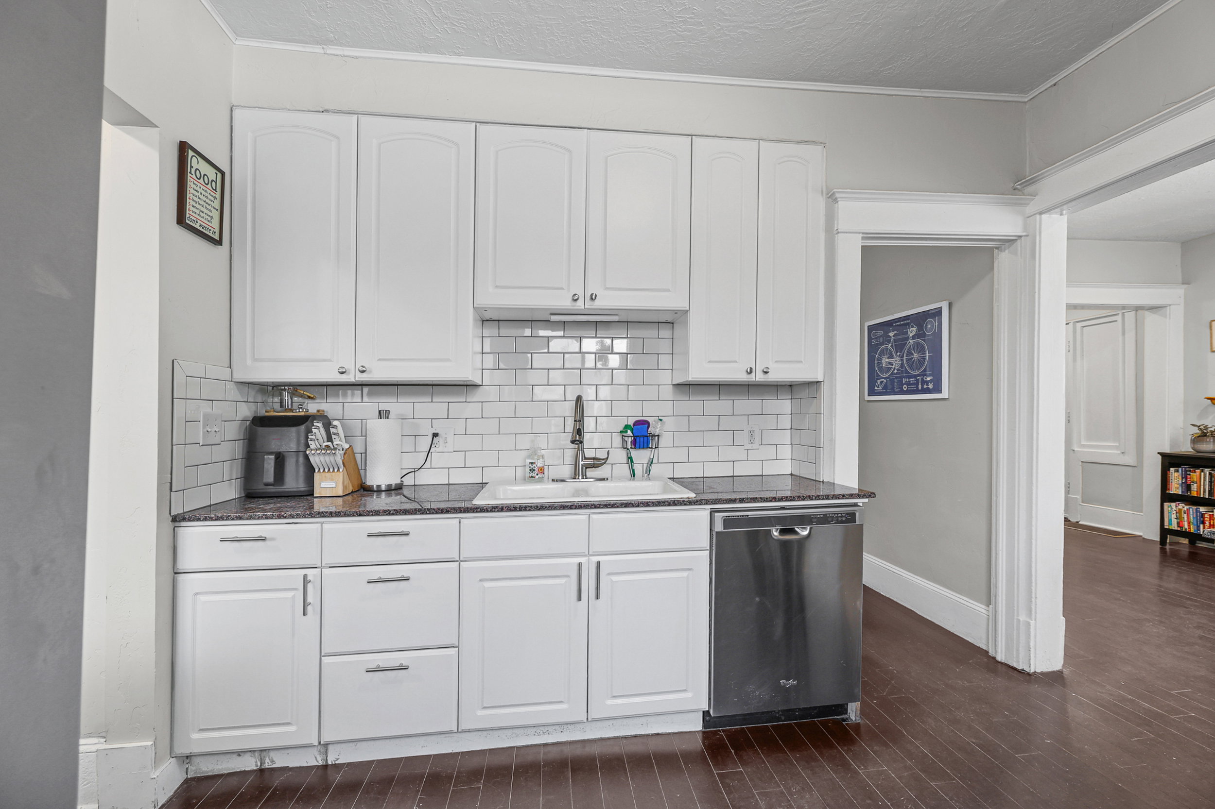 Kitchen featuring white cabinetry, dark countertops, white subway tile backsplash, and a stainless steel dishwasher