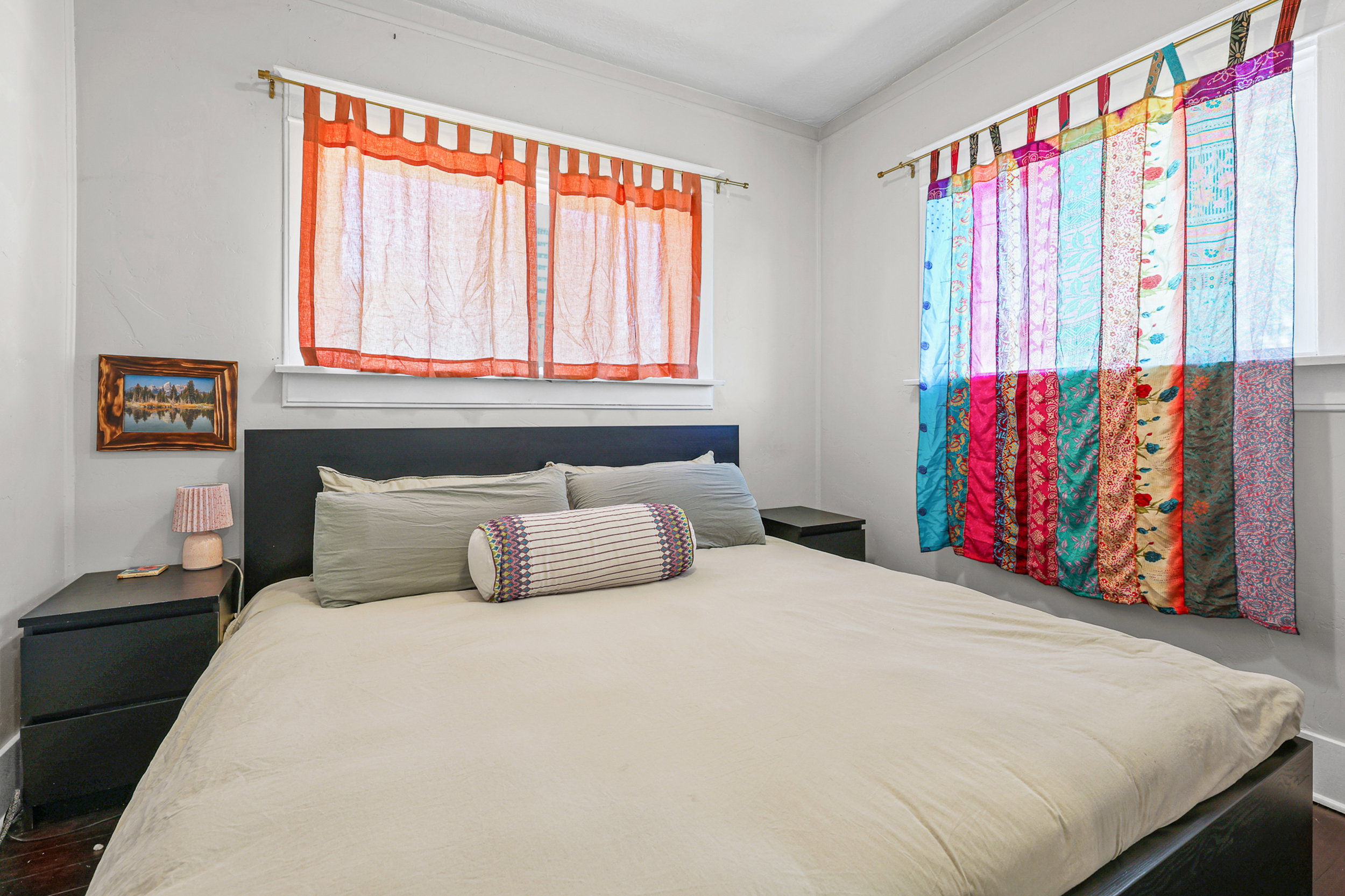 Bright room featuring two windows with natural light, a dark headboard, and wood-finish flooring