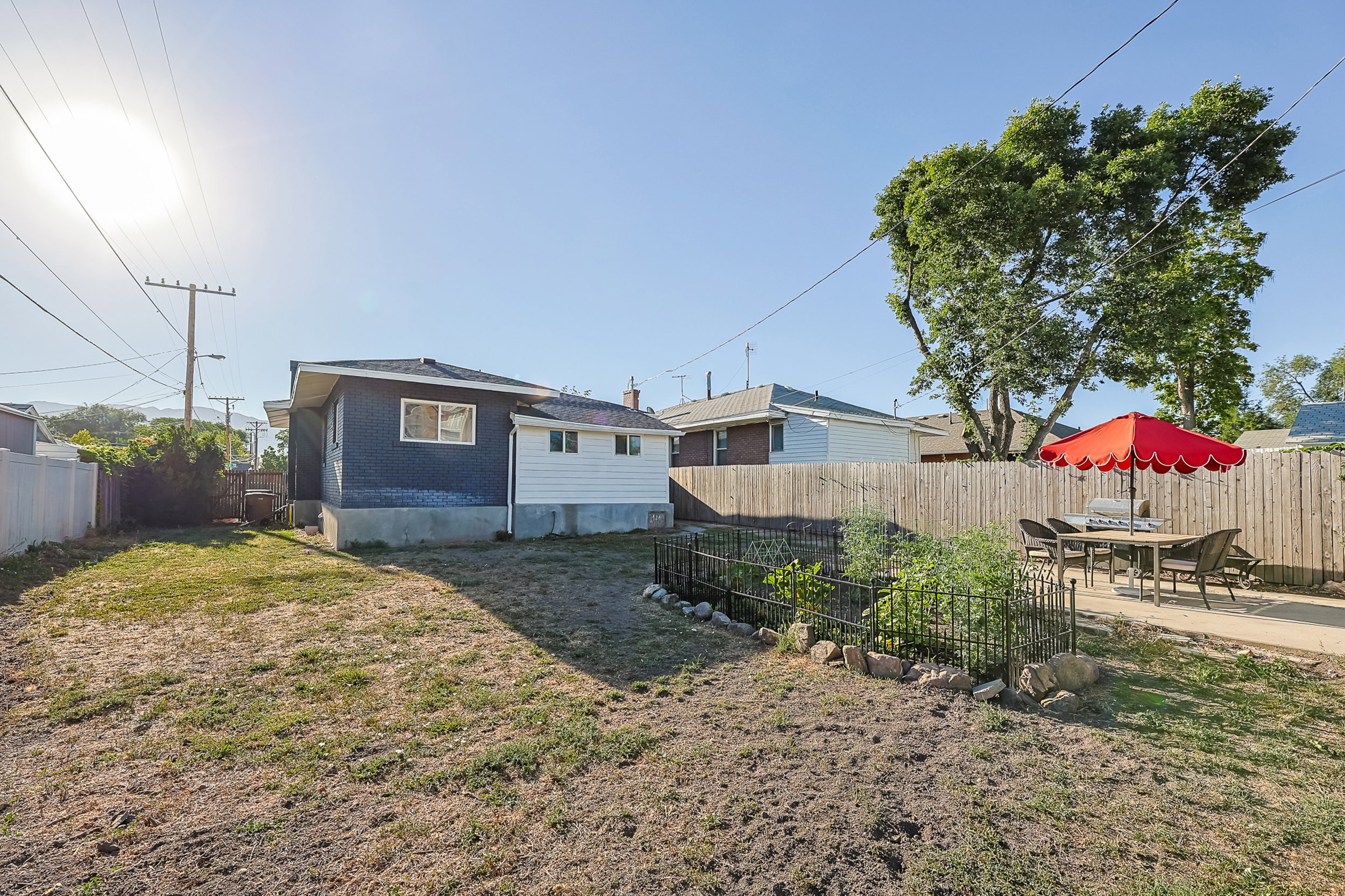 Spacious backyard featuring a concrete patio, wood privacy fencing, and a dedicated garden area with wrought iron fencing