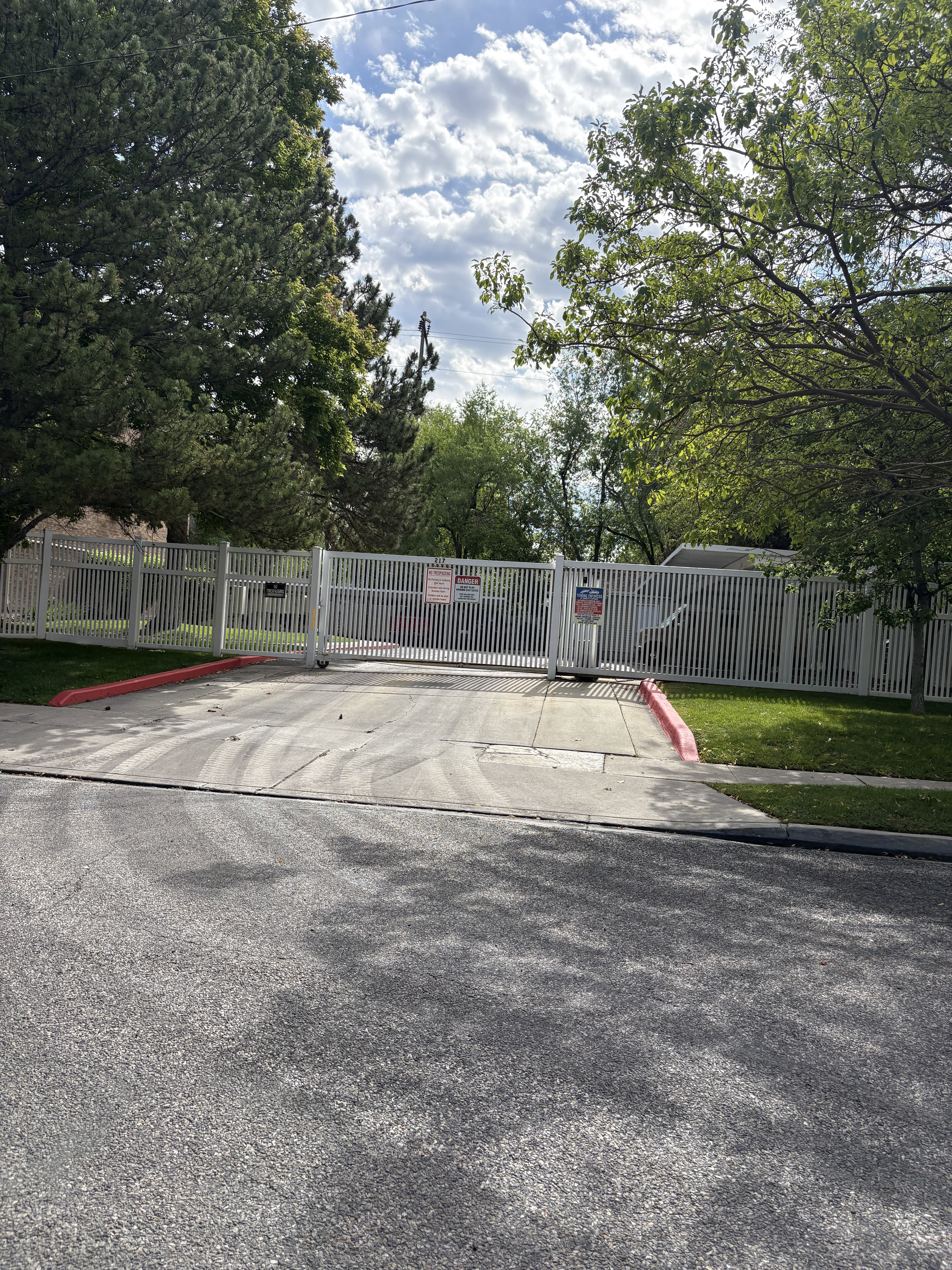 Gated entry with a white metal fence and mature trees