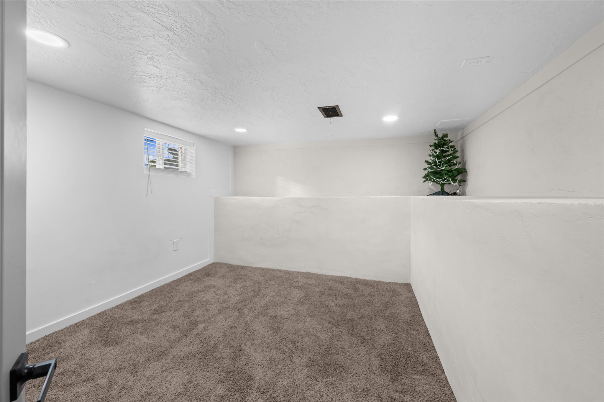 Carpeted lower-level room featuring white walls and a white ceiling with recessed lighting