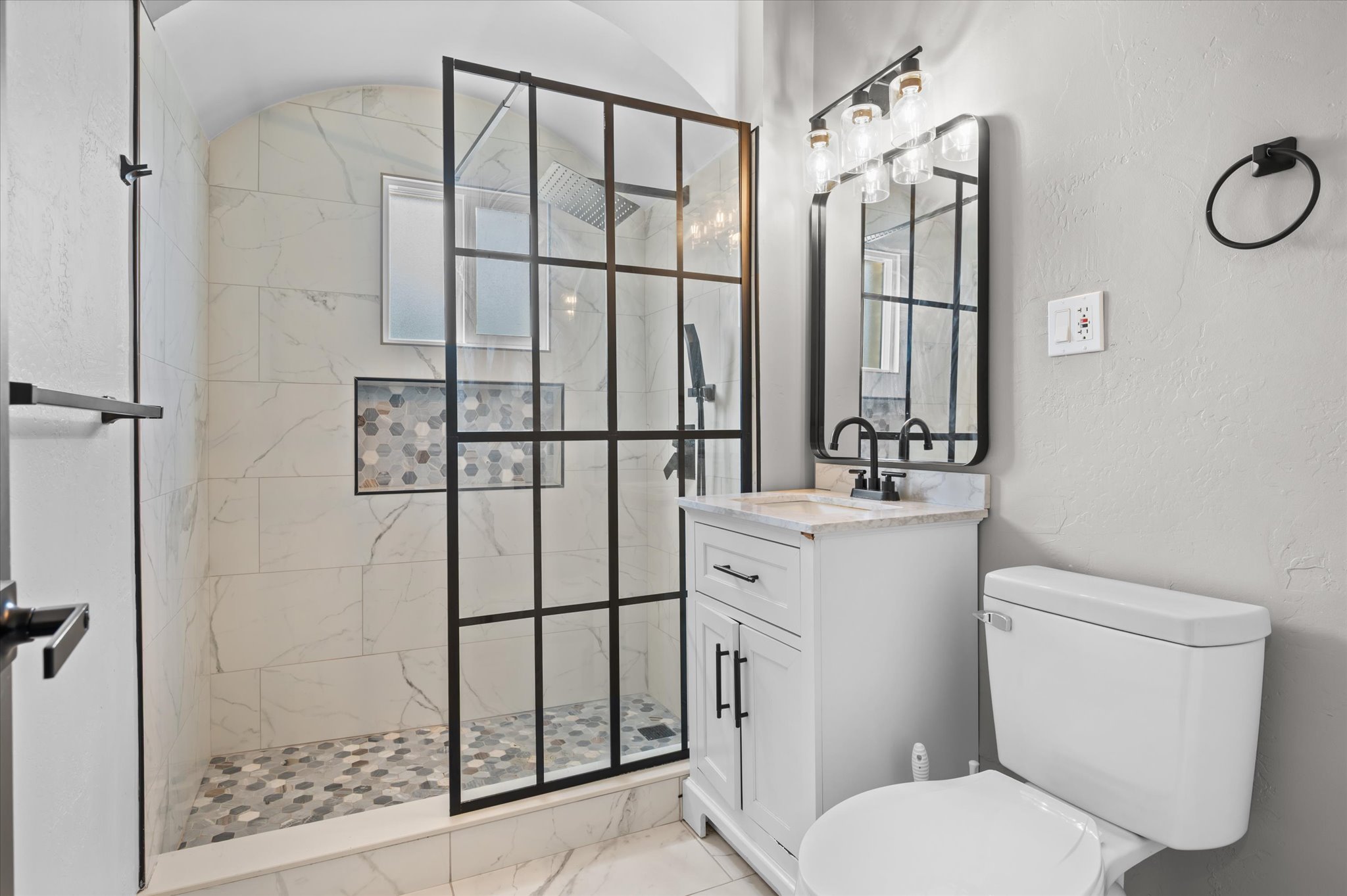 Modern bathroom featuring a walk-in shower with black-framed glass enclosure, white marble-look wall tiling, and a mosaic tiled shower floor