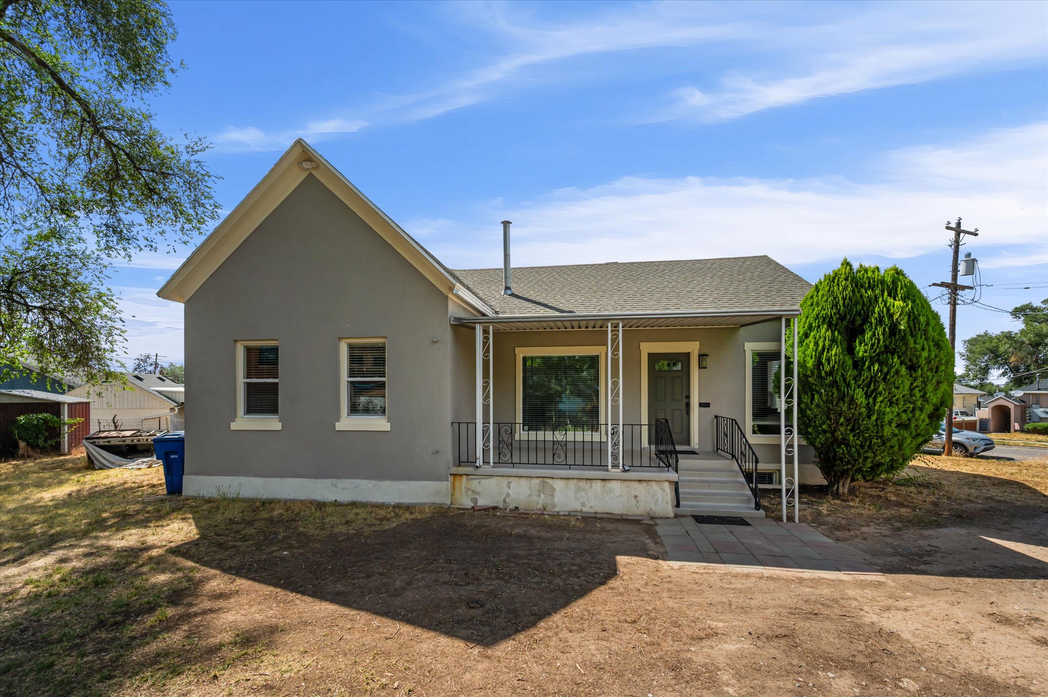 Stucco exterior with a pitched roof, featuring a covered front porch with decorative iron railings