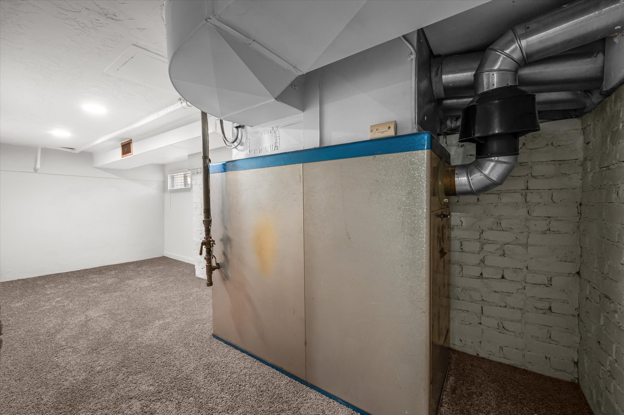 Carpeted lower level room with recessed lighting, painted brick wall, and visible utility infrastructure
