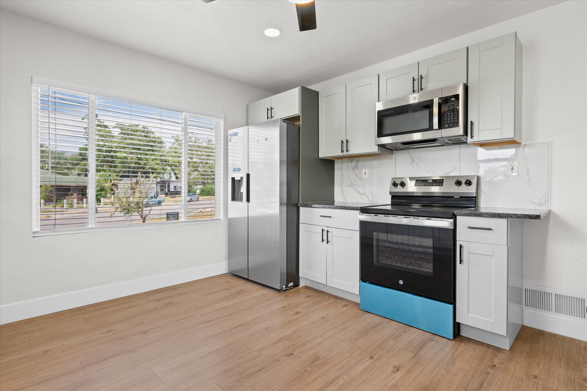 Modern kitchen featuring light gray cabinetry, stainless steel appliances, a white tile backsplash, and dark countertops