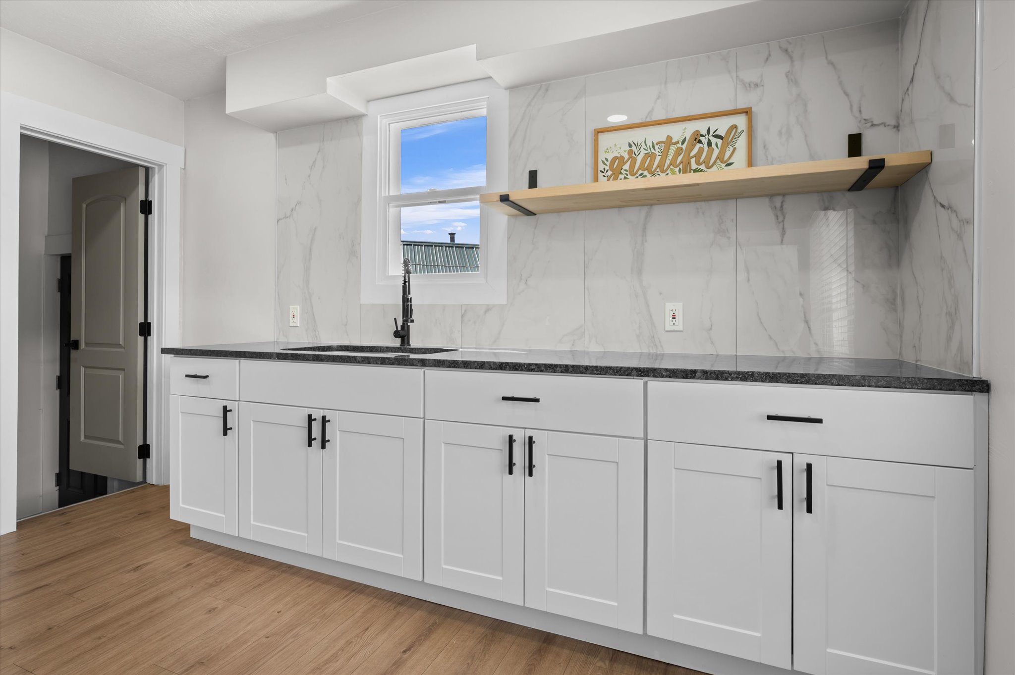 White shaker cabinetry with dark hardware, dark speckled countertops, and a white marble-look tile backsplash