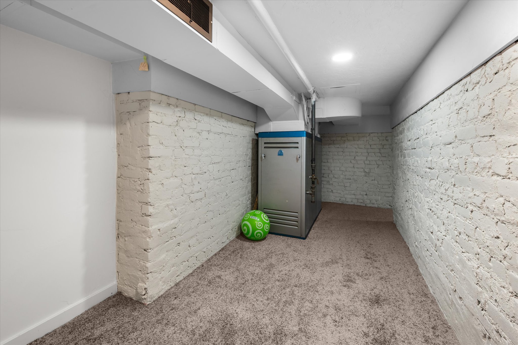 Basement utility space featuring painted brick walls, recessed ceiling lighting, and a neutral carpeted floor