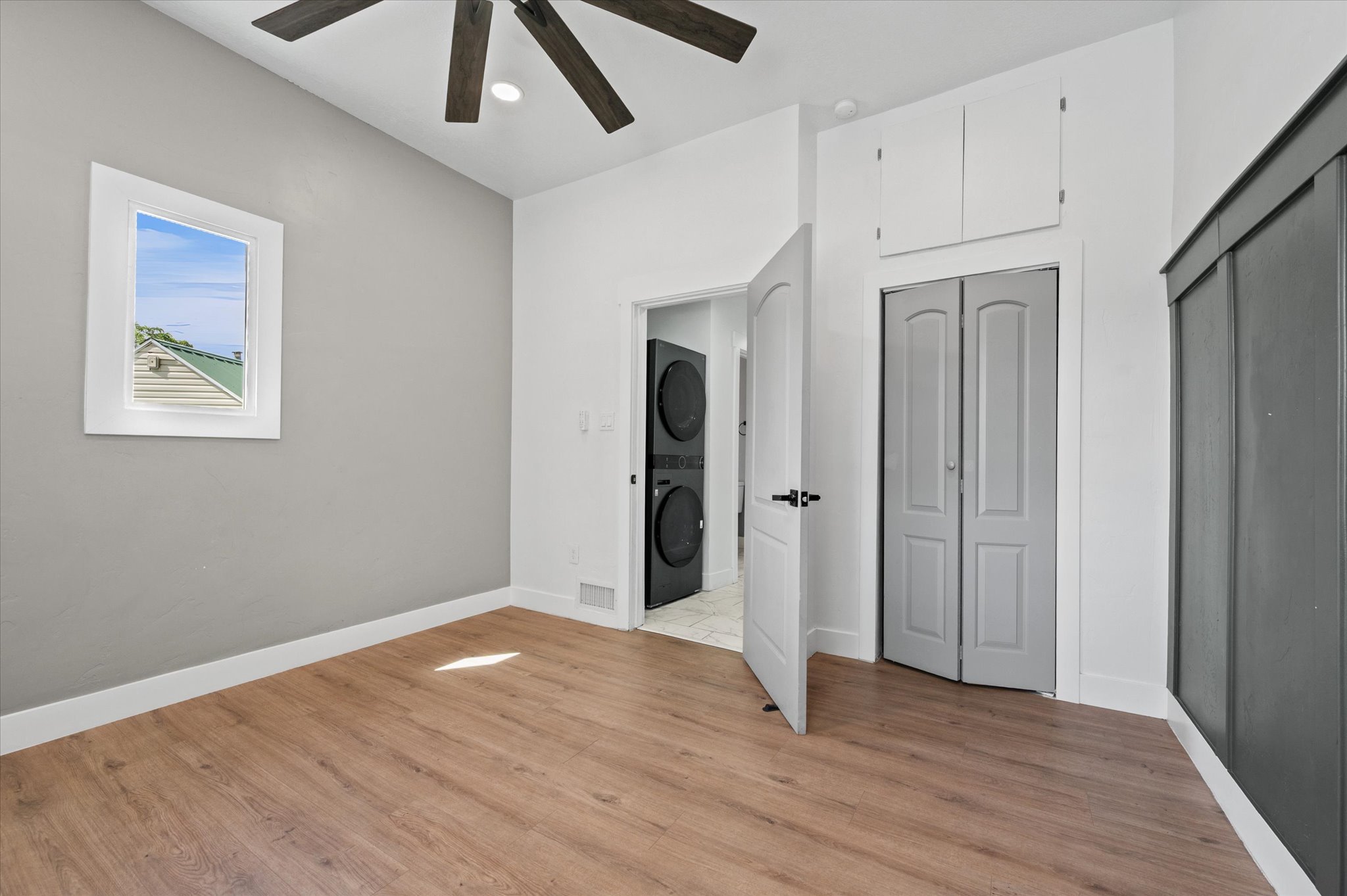 Room featuring wood-finish flooring, a ceiling fan, and a single window with white trim