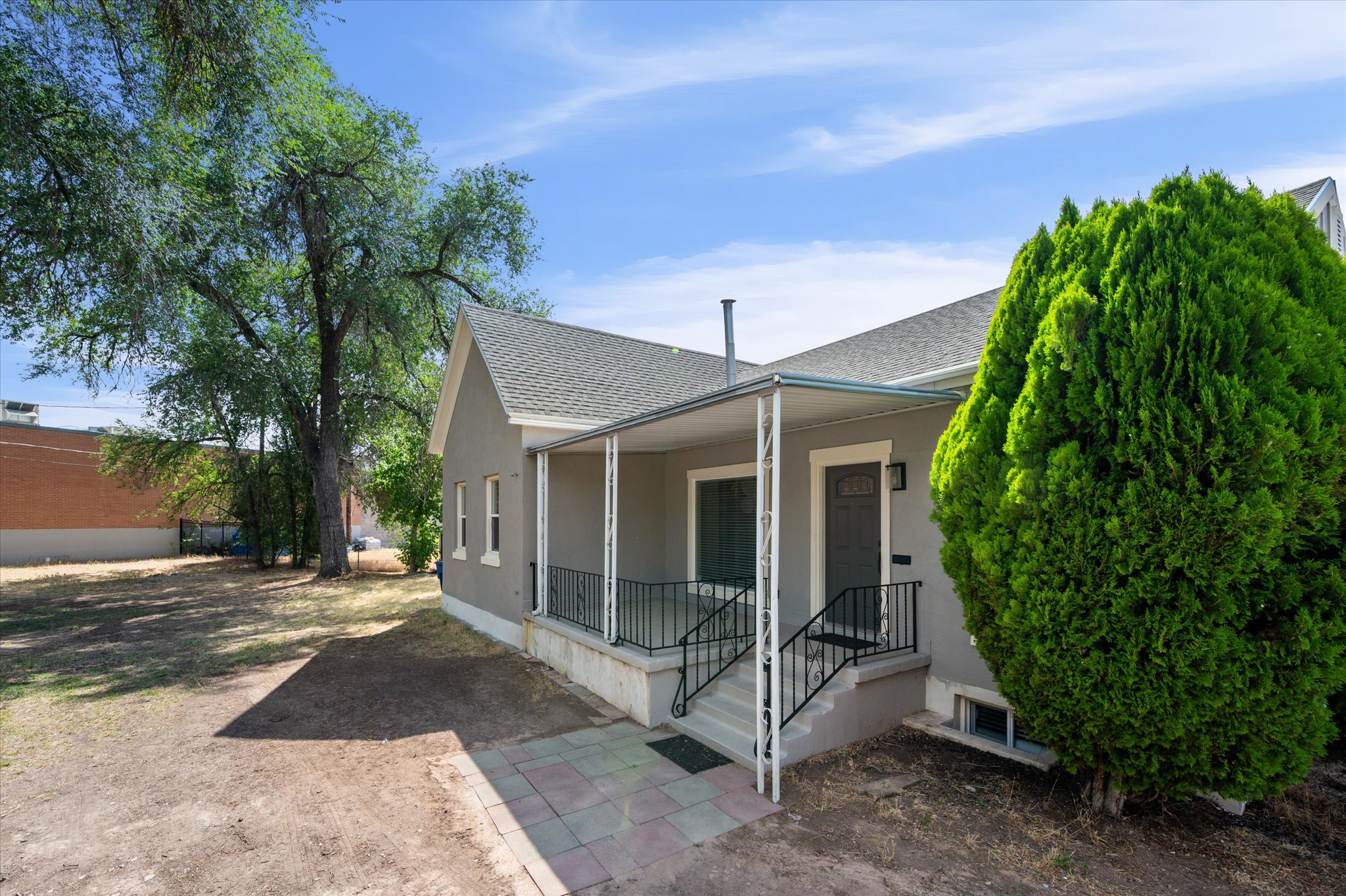 Exterior featuring a covered porch with white columns and black railings, a gray facade, and a dark entry door