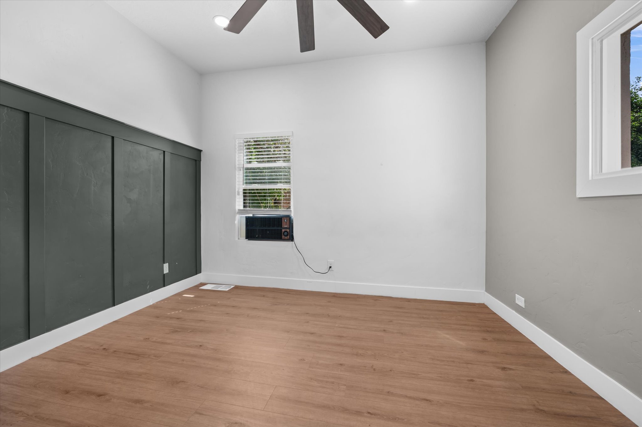 Room featuring wood-finish flooring, a contemporary ceiling fan, and a prominent dark accent wall with vertical paneling