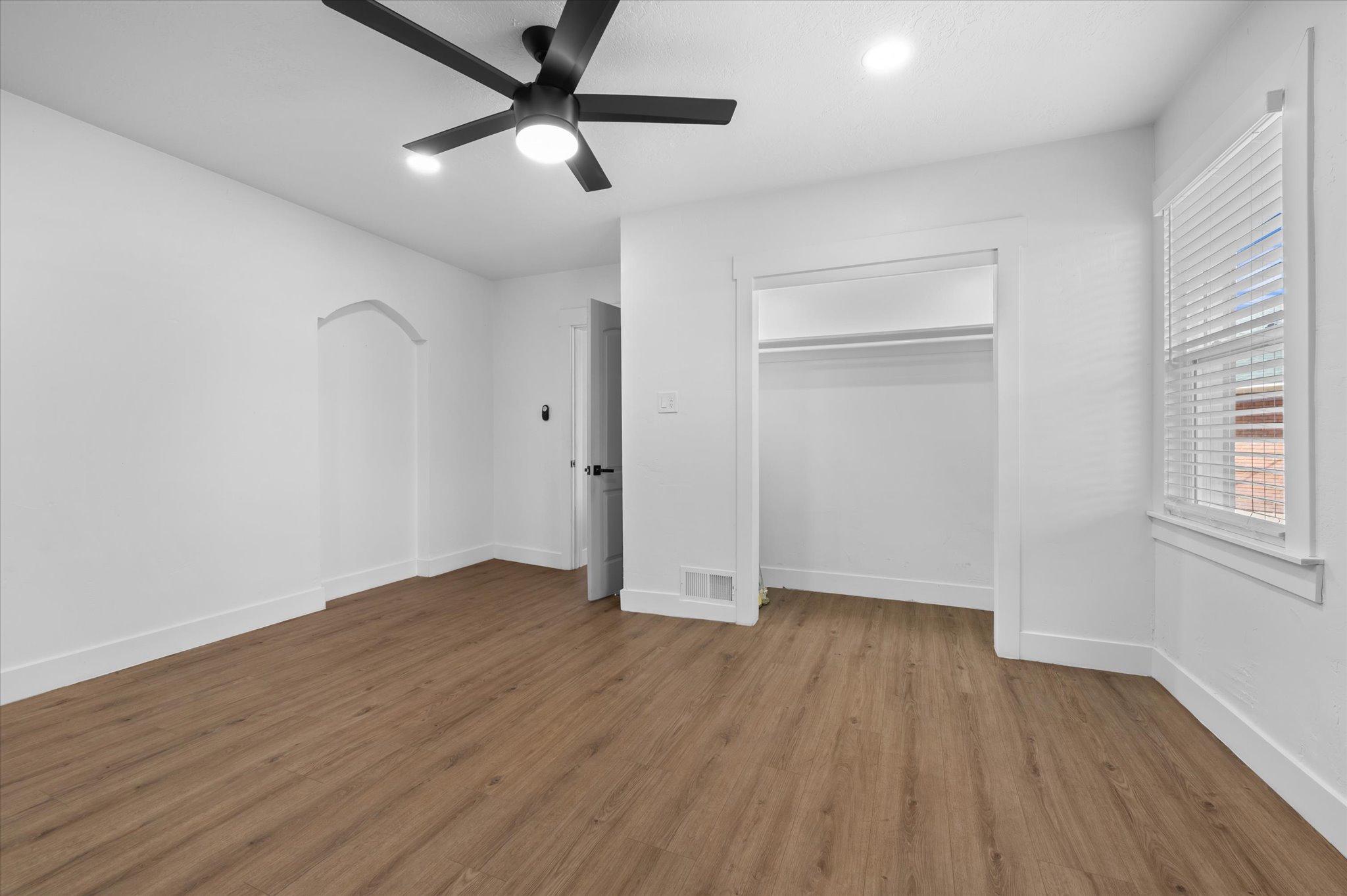 Spacious room featuring wood-finish flooring, white walls, and a modern black ceiling fan with integrated lighting