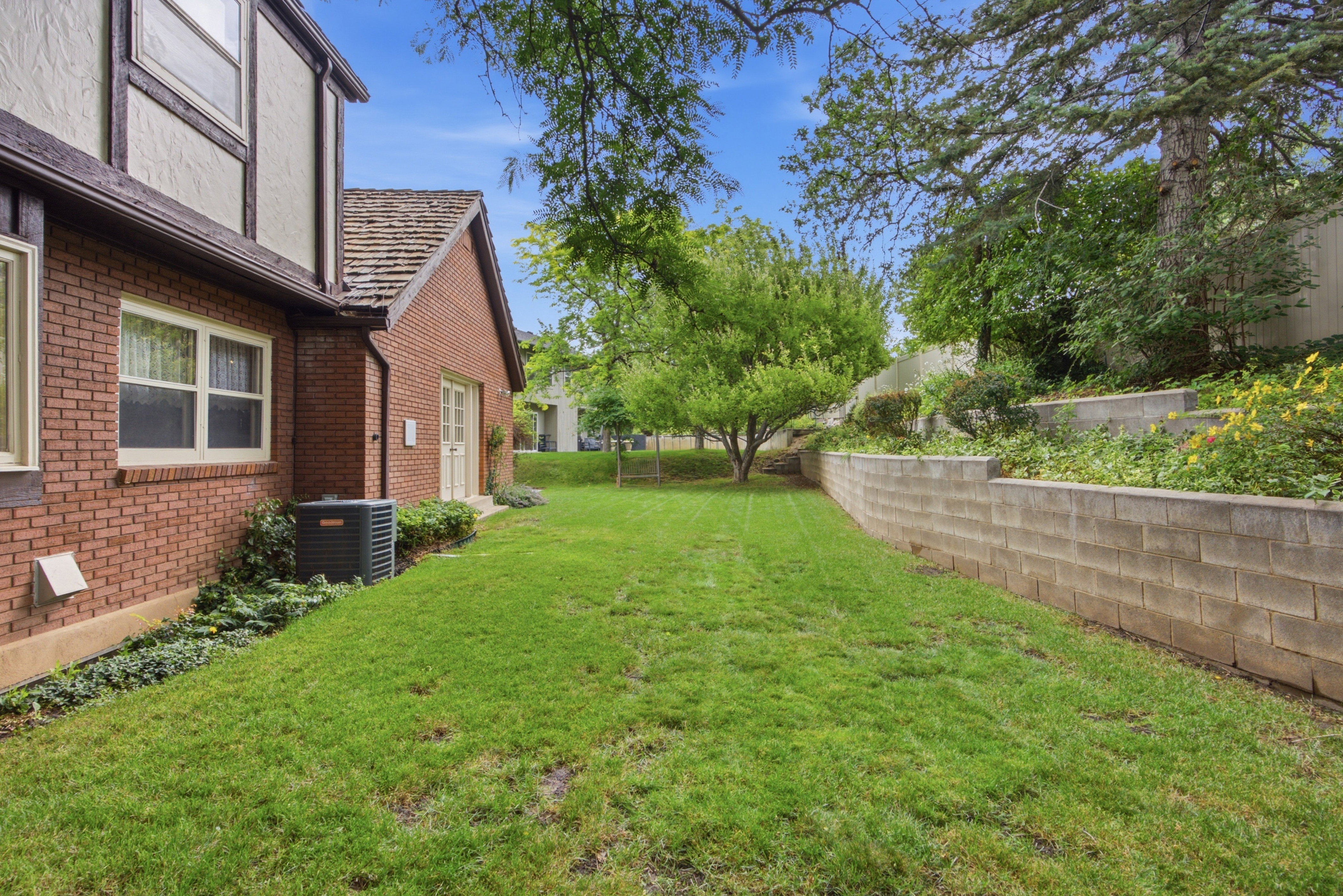 Expansive grassy lawn bordered by tiered retaining walls and mature trees