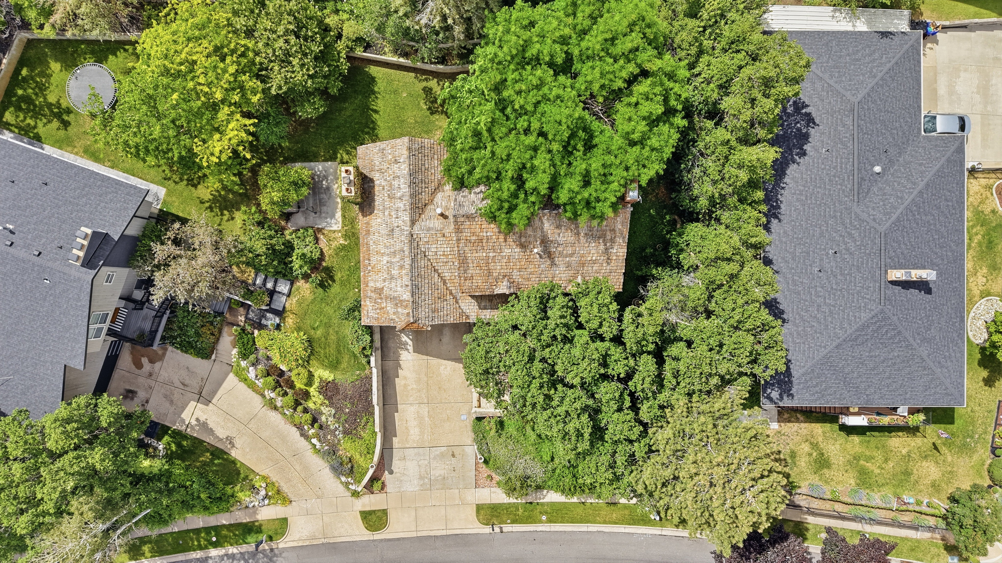 Aerial perspective showcasing a property featuring a multi-gabled roof, mature landscaping, a paved driveway, and a spacious green lawn