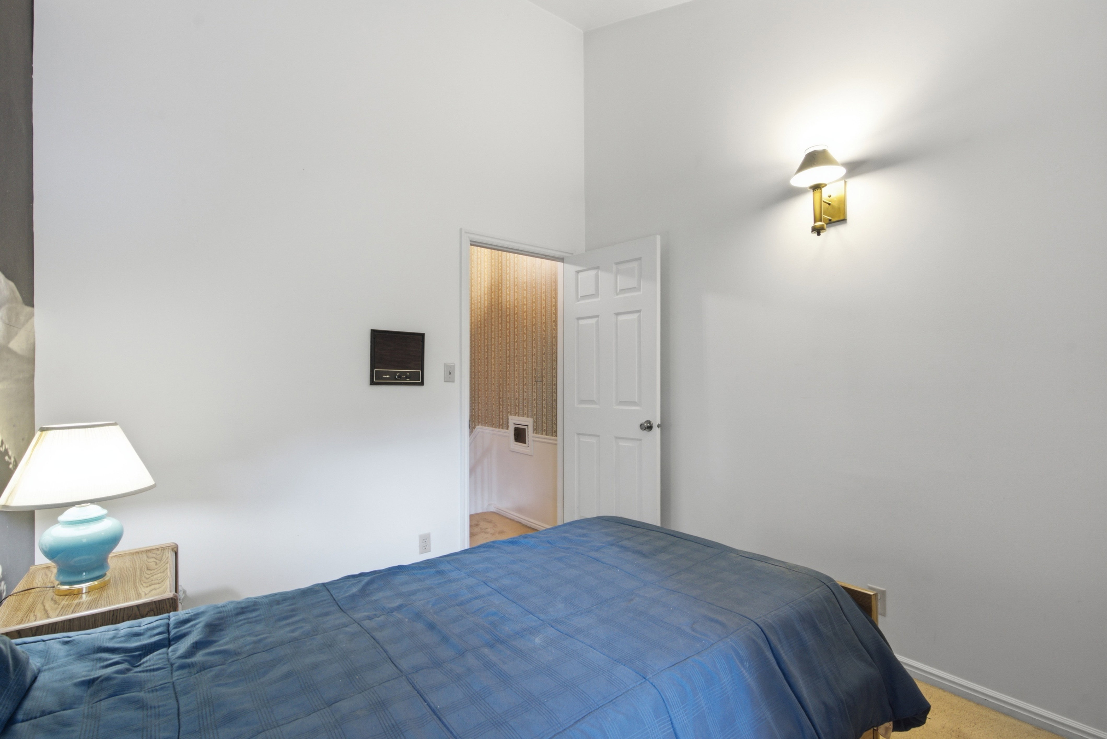White painted walls with a vaulted ceiling, wood-finish flooring, and a wall-mounted sconce