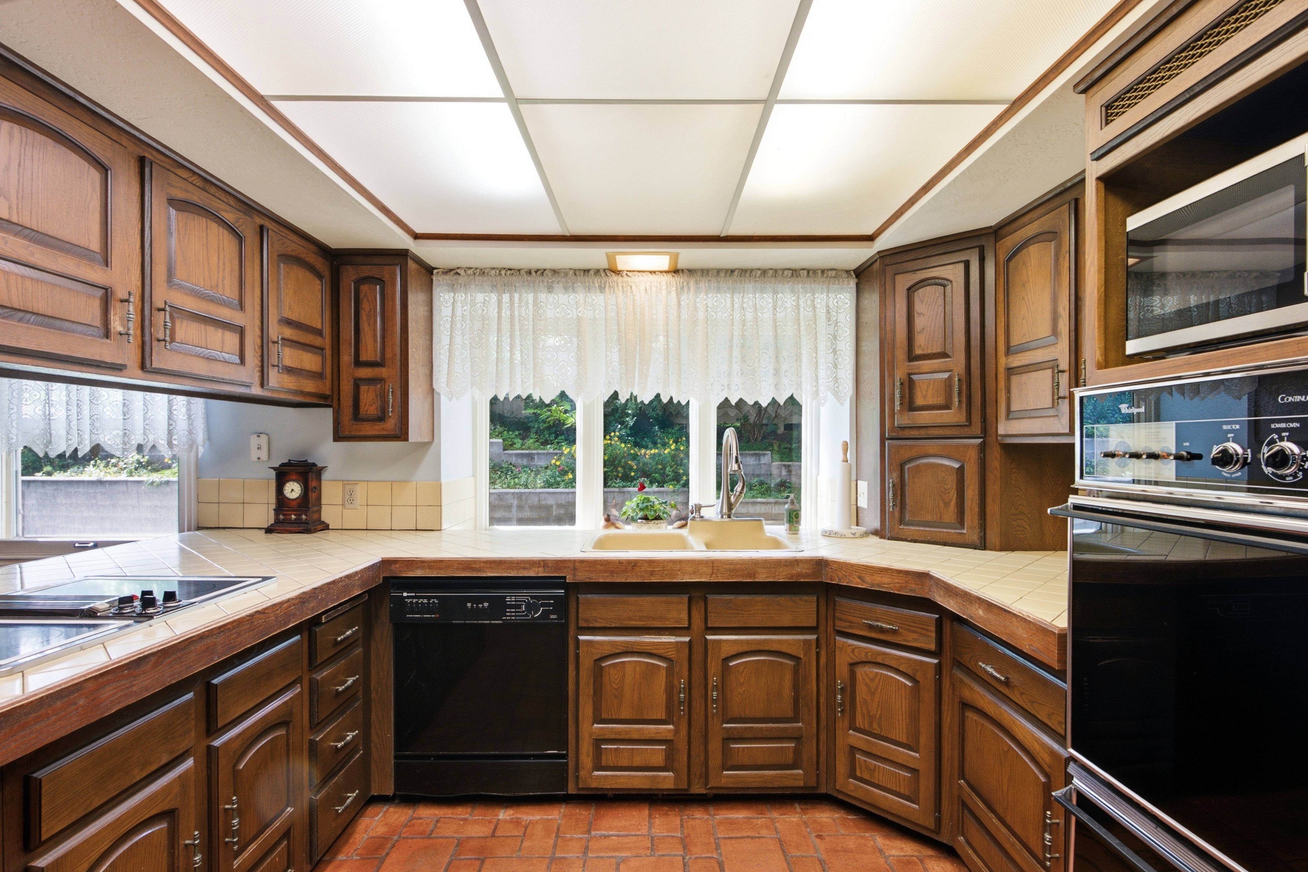 Kitchen featuring abundant wood cabinetry, integrated oven, built-in microwave, tile countertops, and terracotta tile flooring