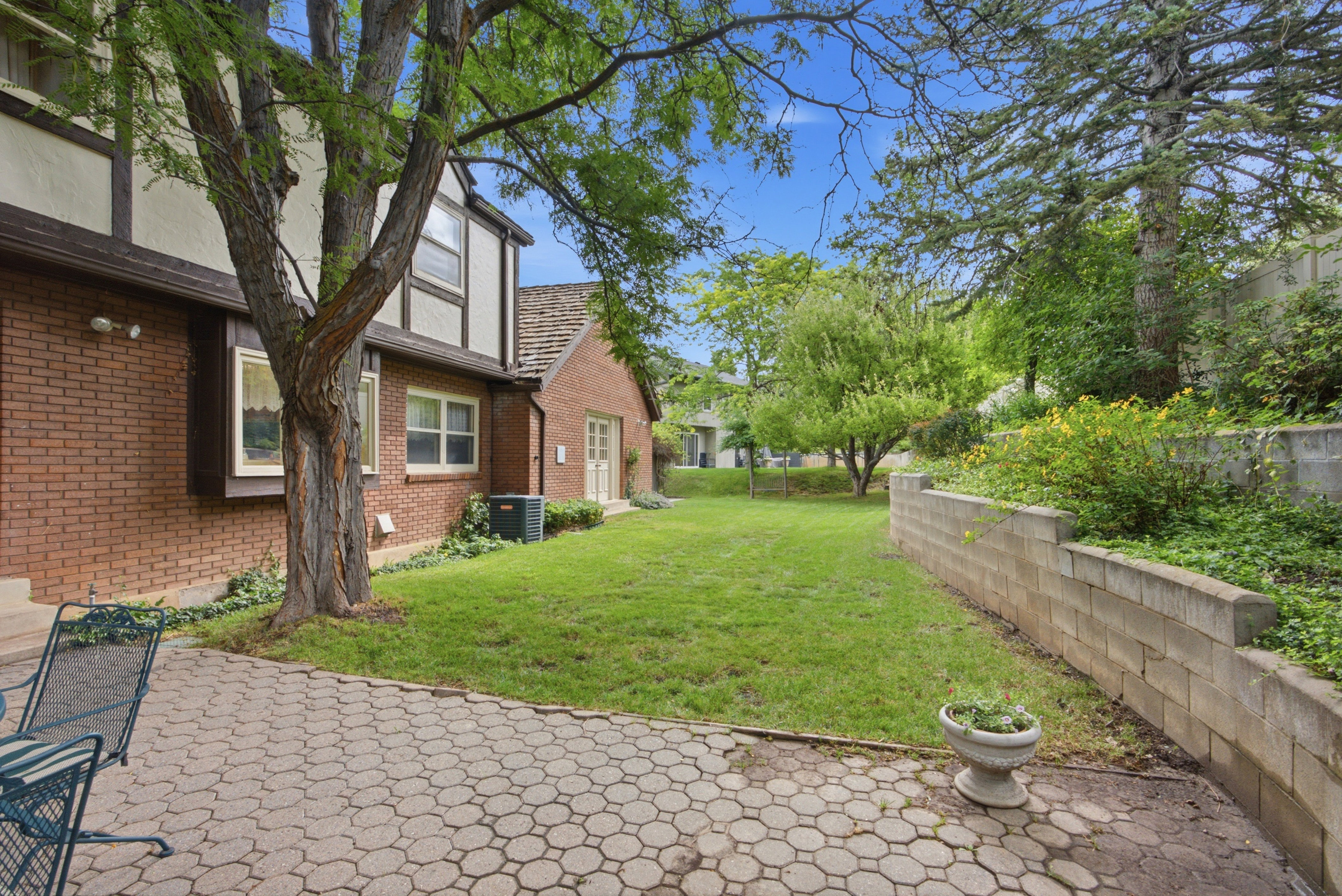 Expansive backyard featuring a patterned paver patio, a manicured lawn, and a multi-level retaining wall with established plantings
