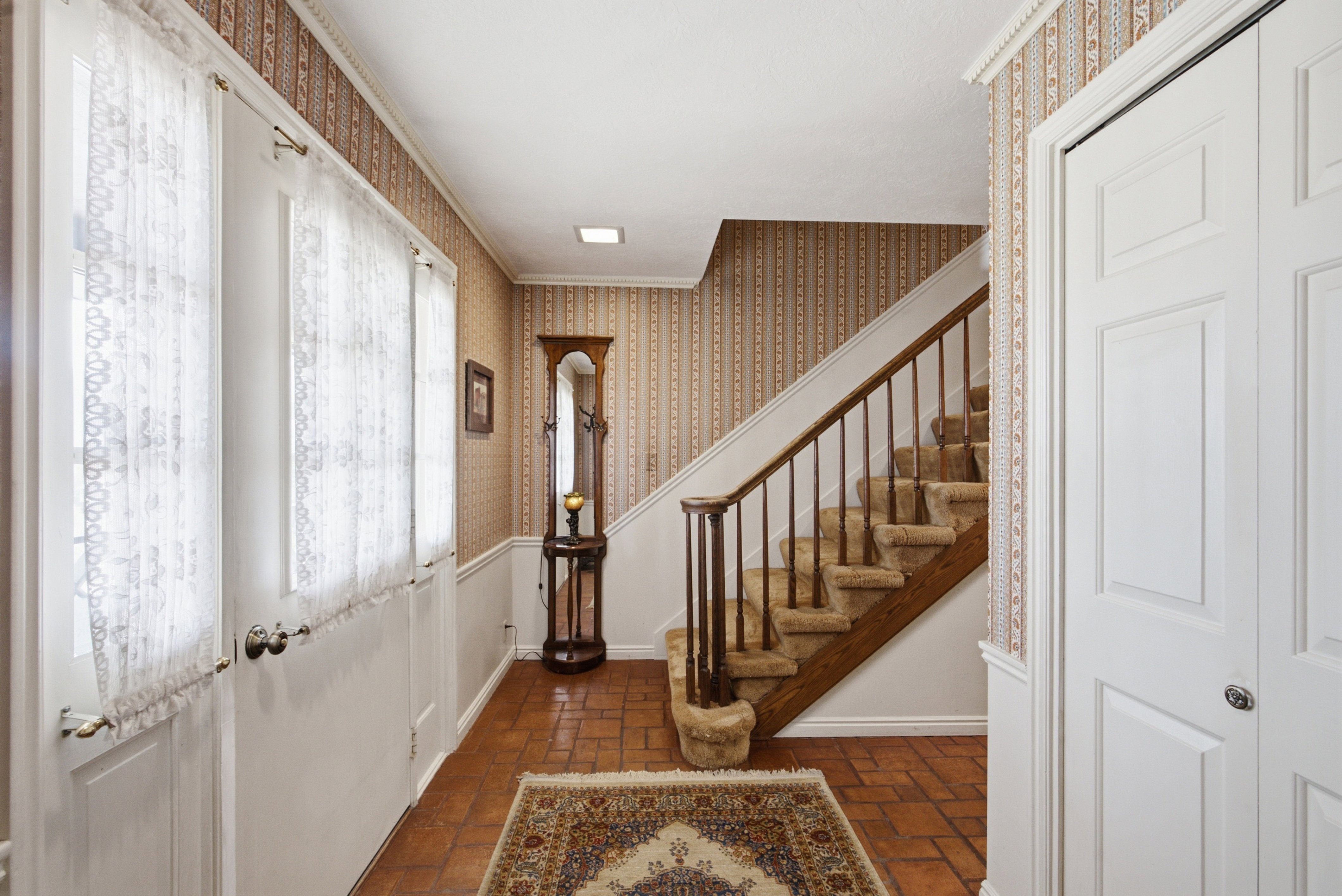 Entryway featuring terracotta-style tile flooring and a carpeted staircase with wood handrails