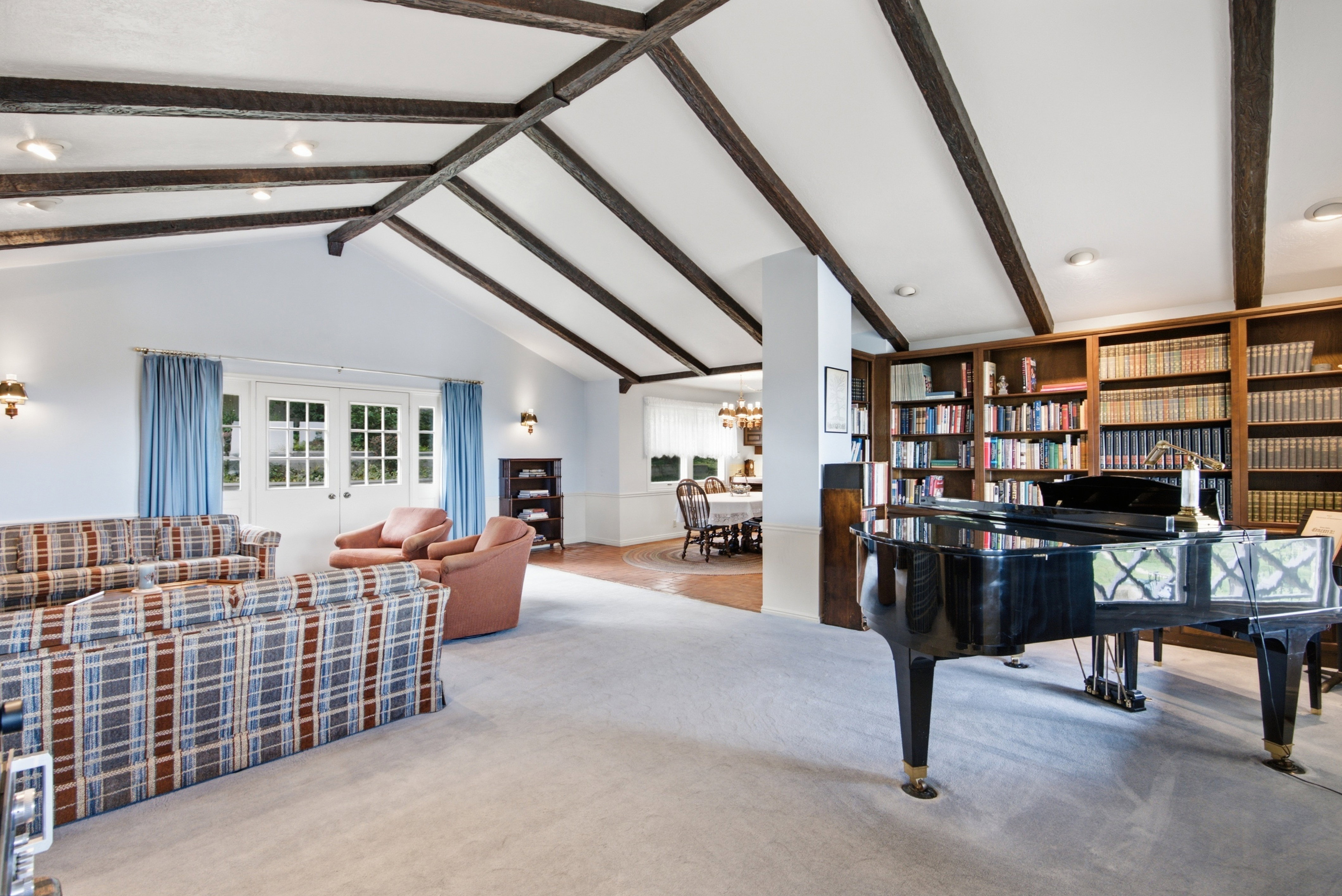 Spacious living area featuring a vaulted ceiling with exposed wood beams, recessed lighting, and wall-mounted sconces