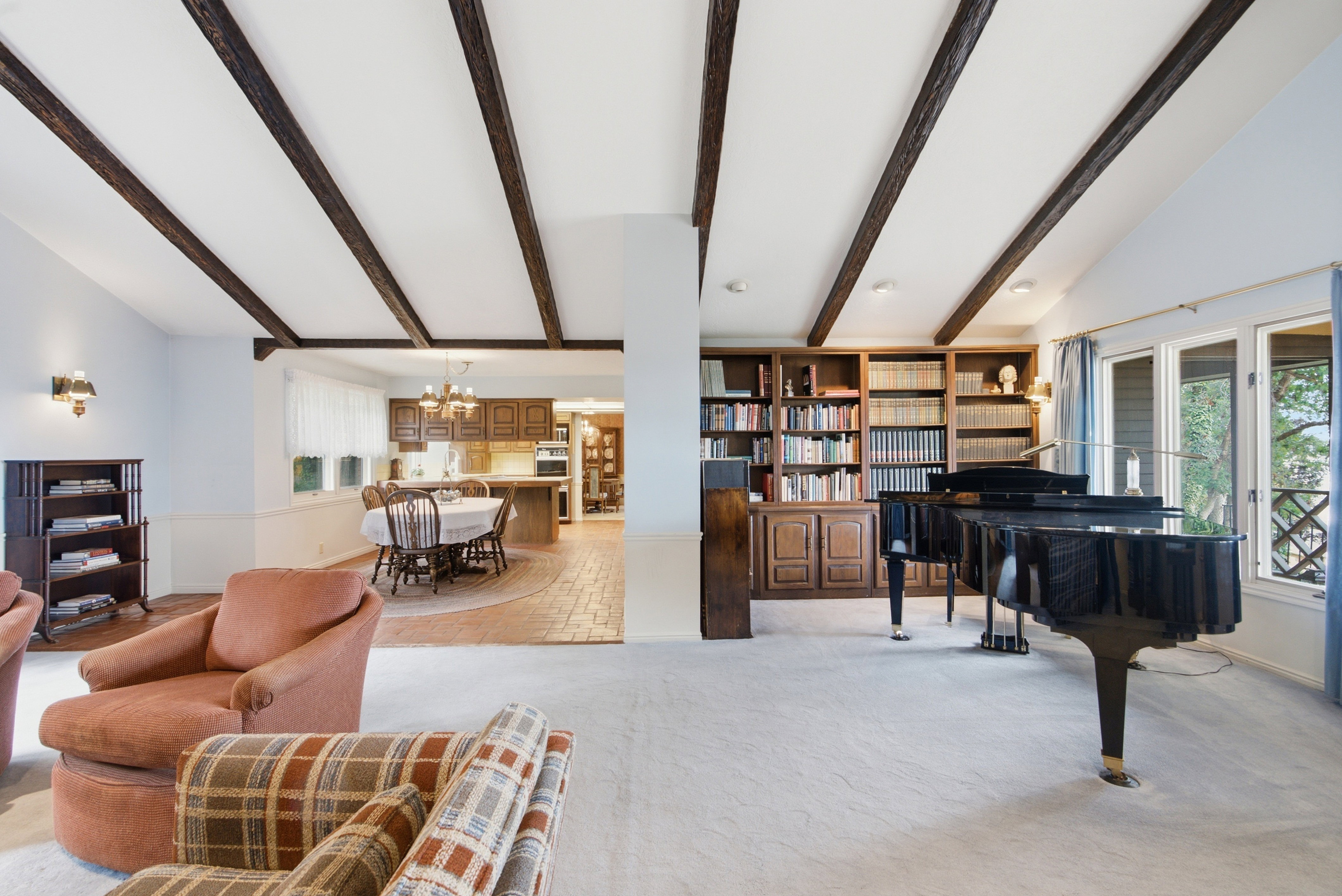 Vaulted ceilings with exposed wood beams define this expansive room, featuring built-in shelving, large windows, and a brick-patterned flooring section