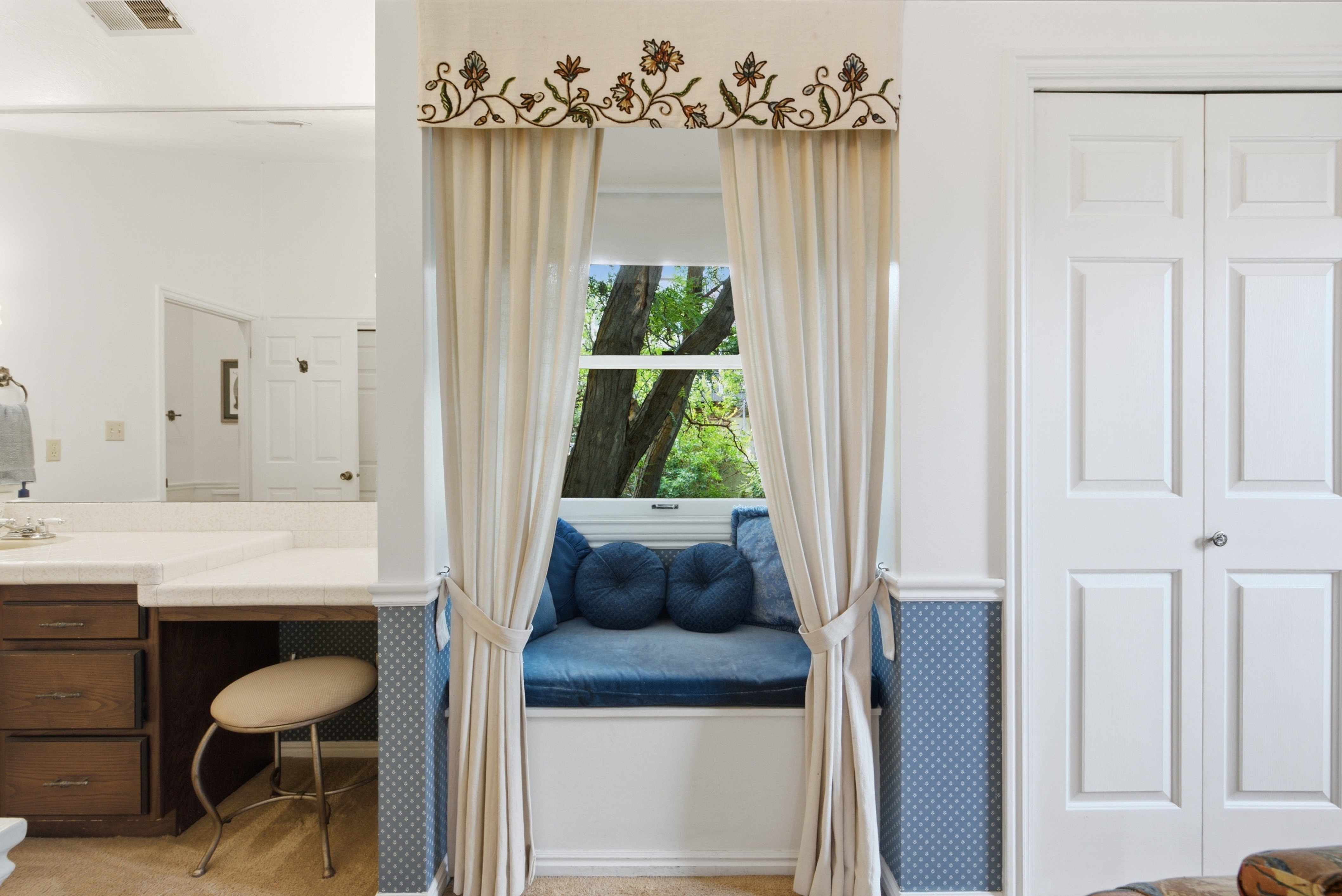 Built-in window seat with a cushioned surface, side panels, custom valance, and soft drapery