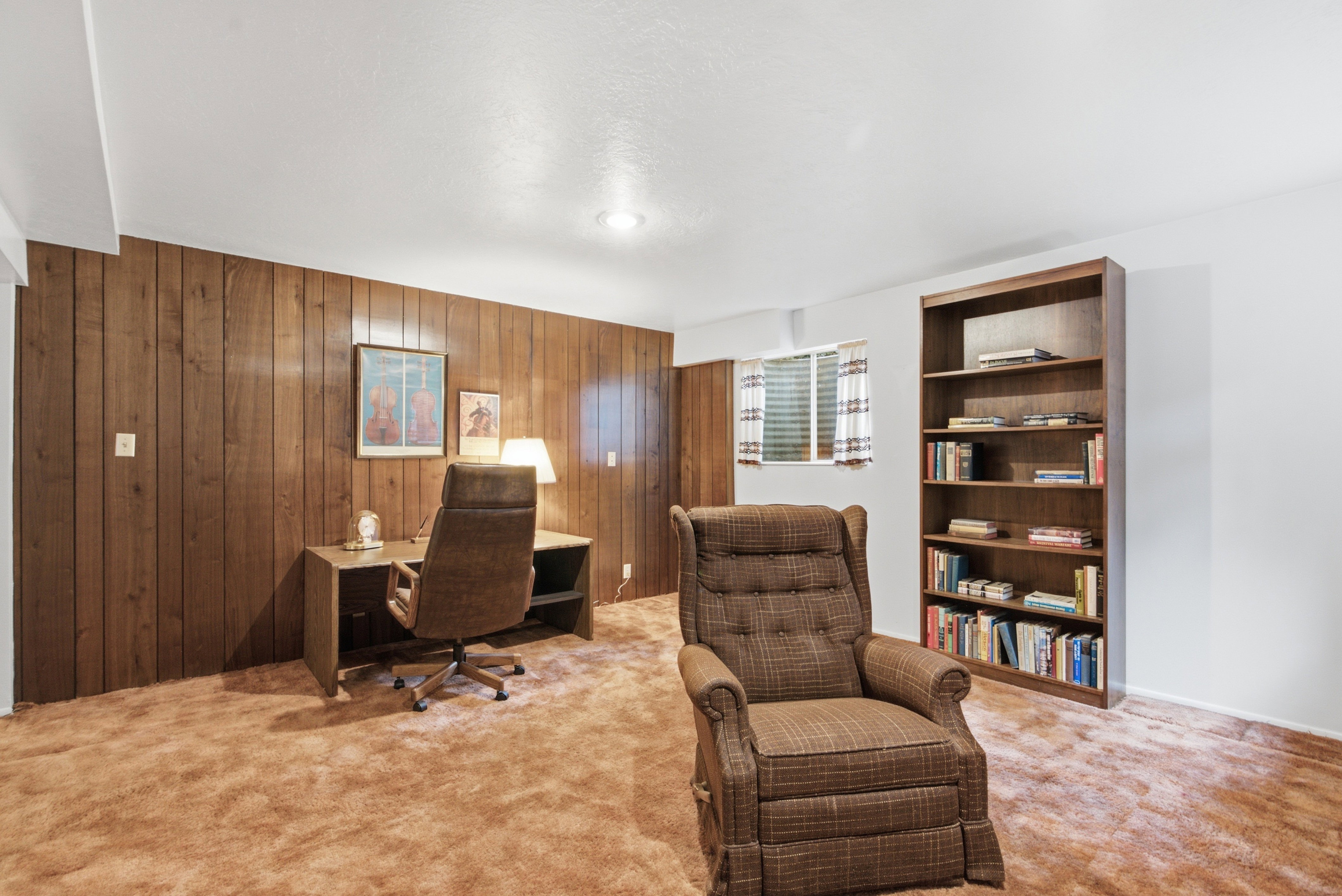 Room featuring wood paneling accent wall, white painted walls, and brown carpeting