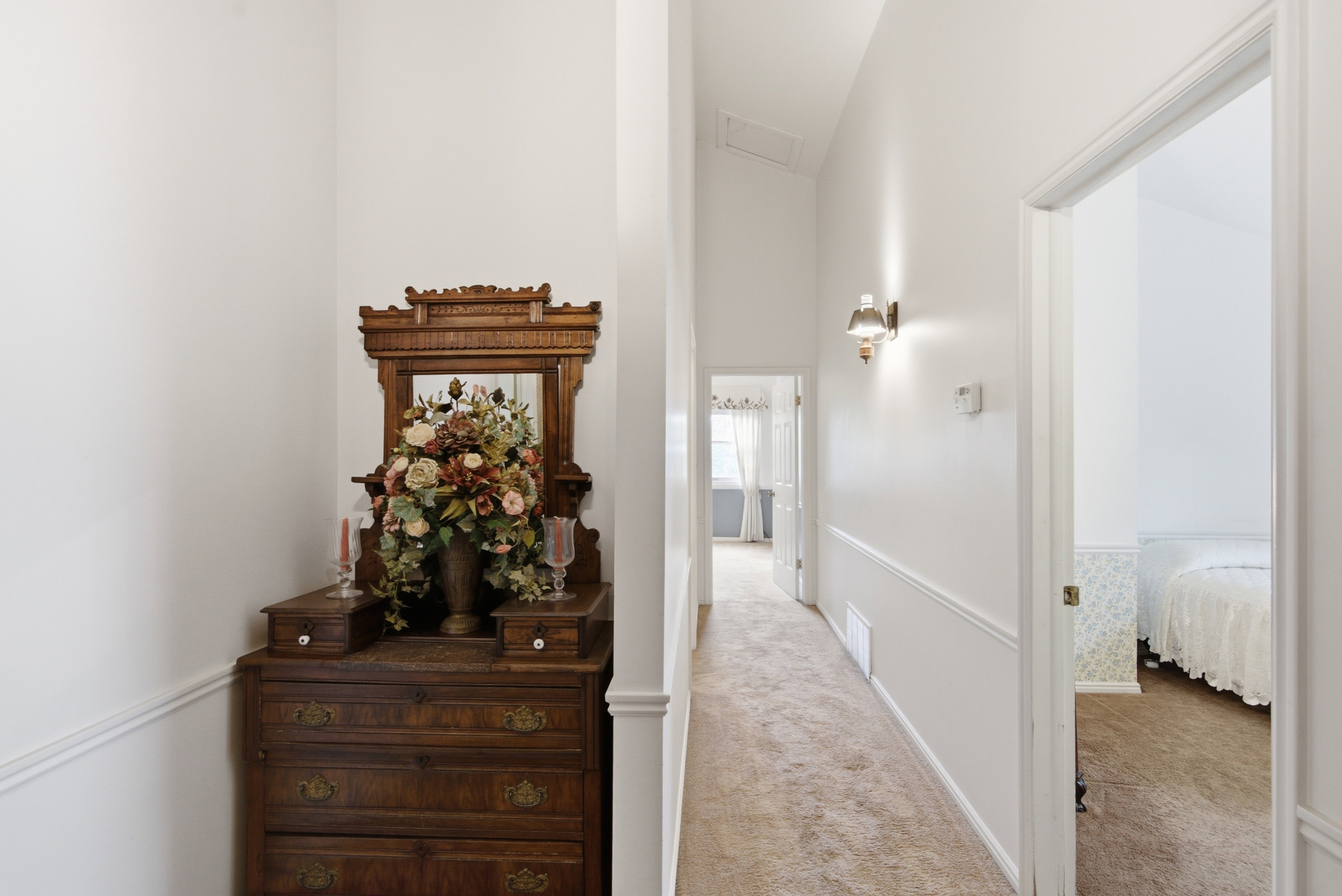 Carpeted hallway with white walls, chair rail molding, and wall-mounted lighting