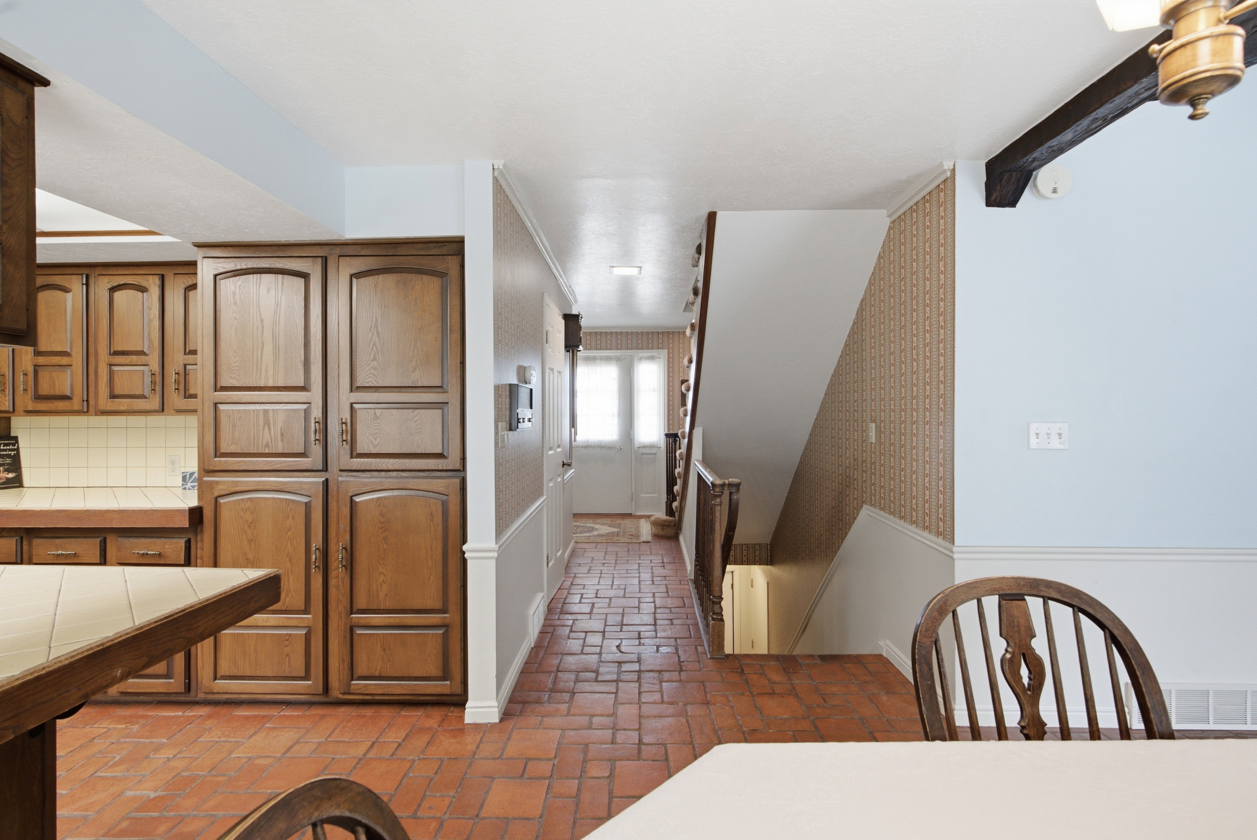 Hardwood cabinetry with ample storage, tile countertops, brick-finish flooring, and a traditional staircase with wood railing