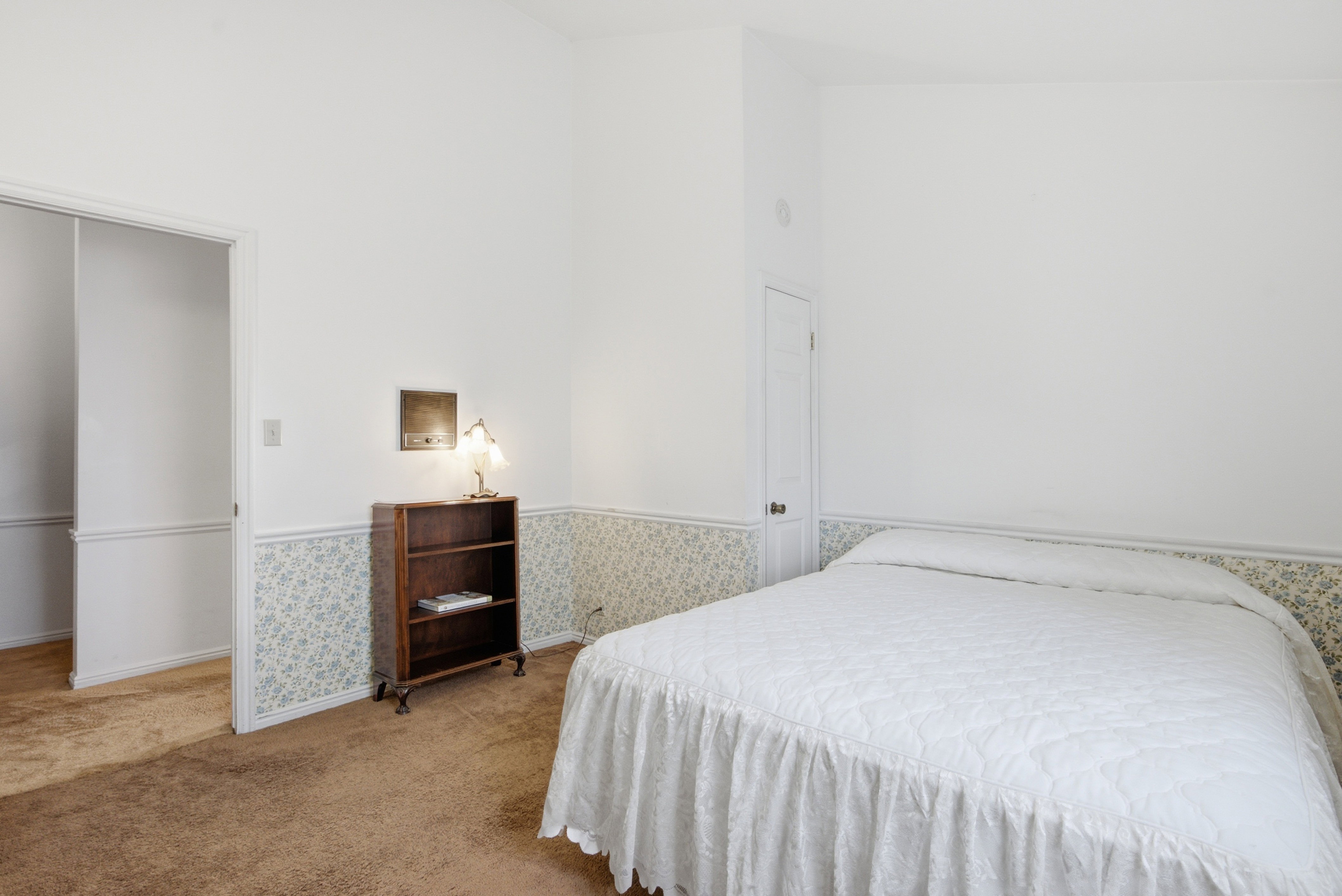 Room featuring white walls above a floral wallpaper border, brown carpet flooring, and white trim