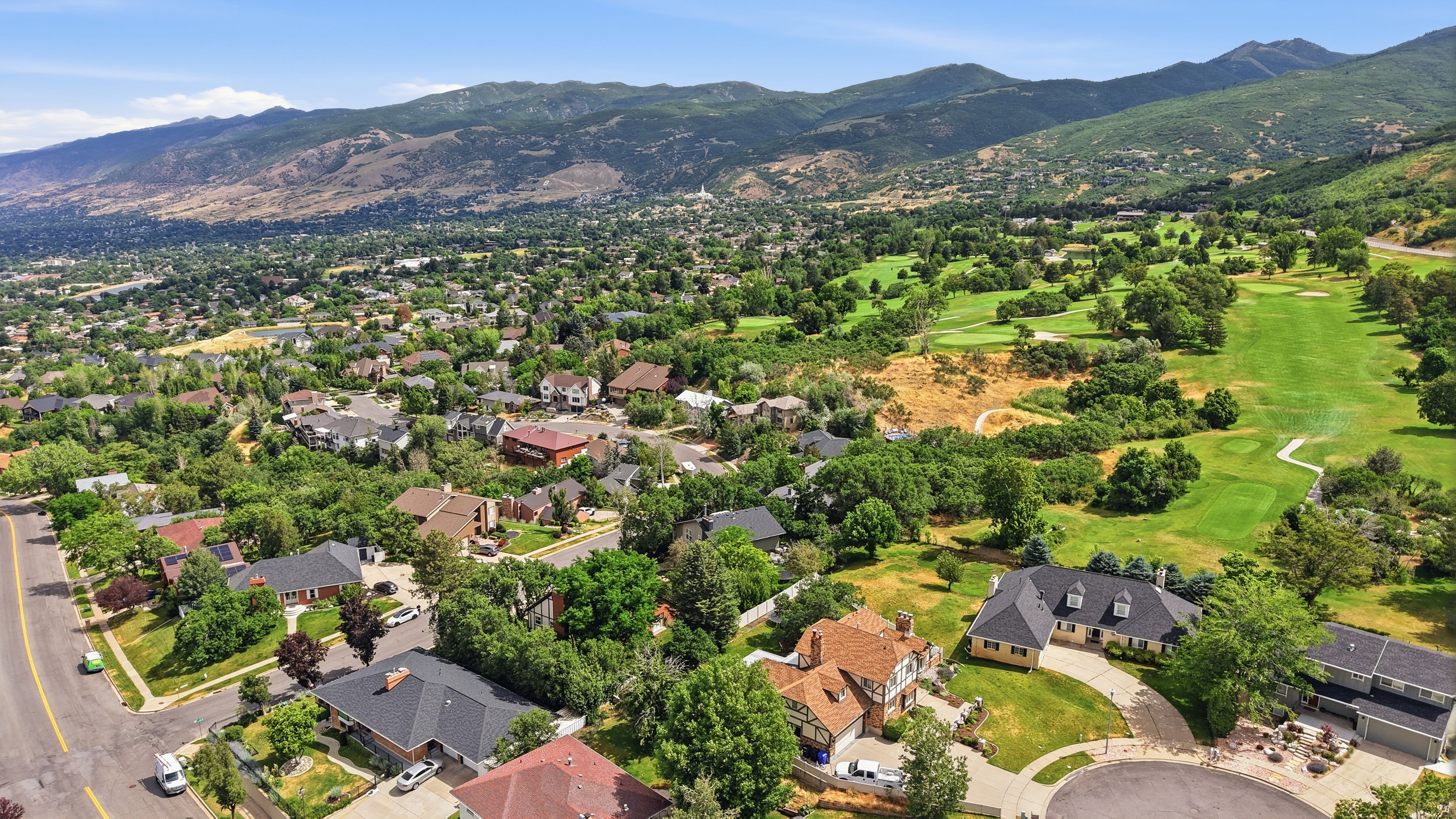Aerial perspective showcasing a residential area with varied architectural styles, a prominent golf course, and a mountain backdrop