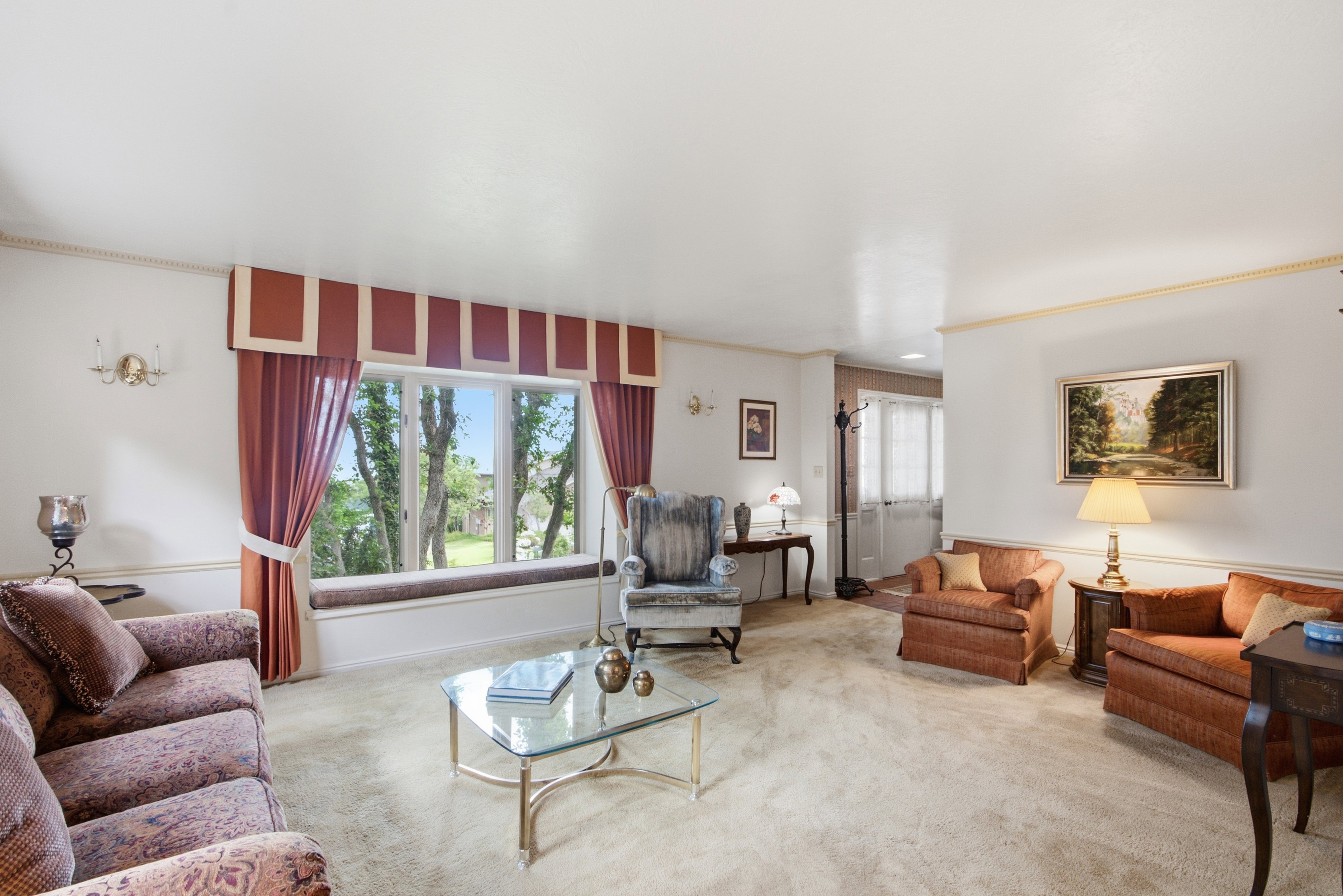 Living area featuring wall-to-wall carpeting, a large bay window with a built-in window seat, crown molding, and wall sconces