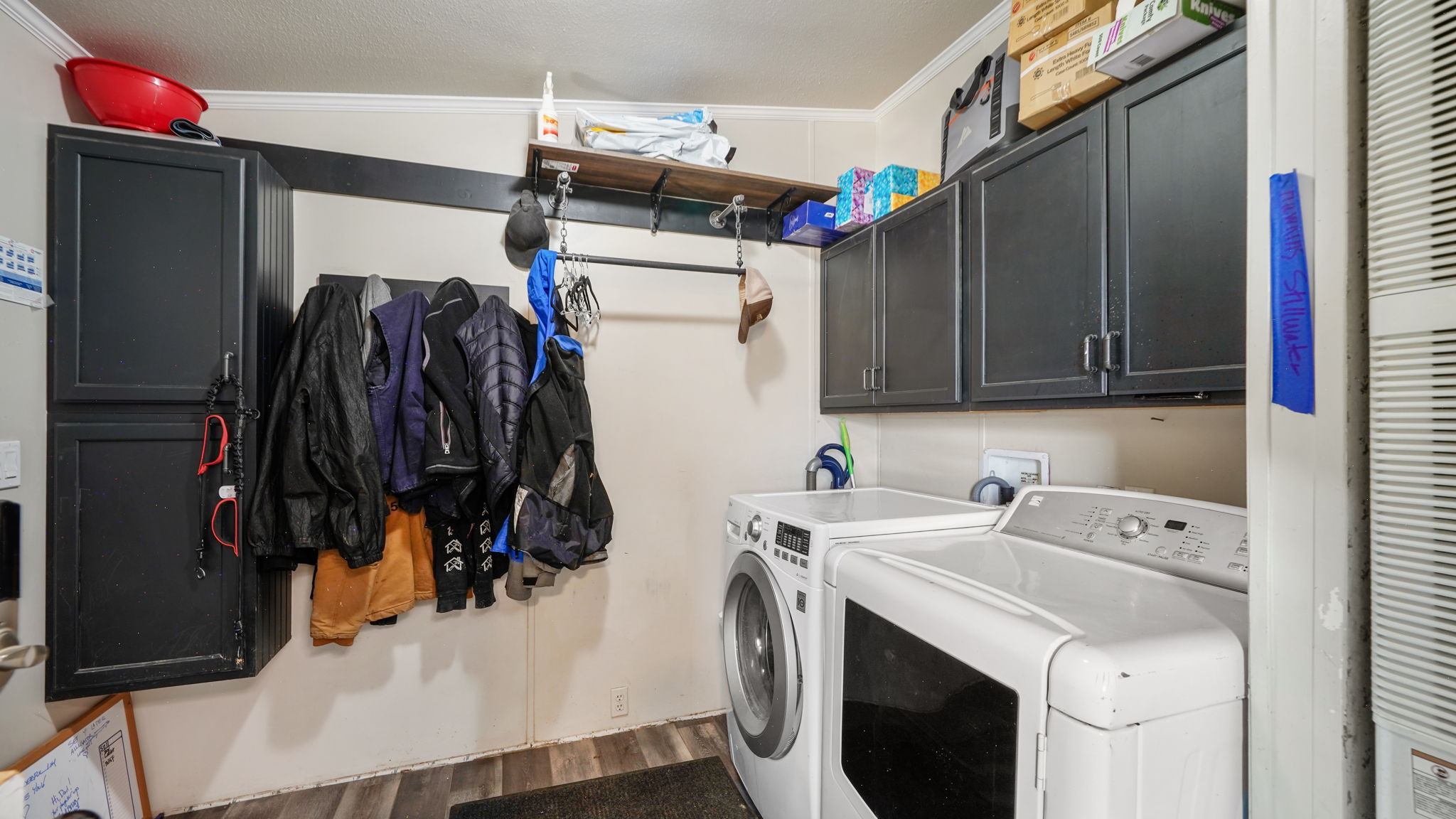 Dedicated utility area featuring wood-finish flooring, white paneled walls, and overhead dark cabinetry