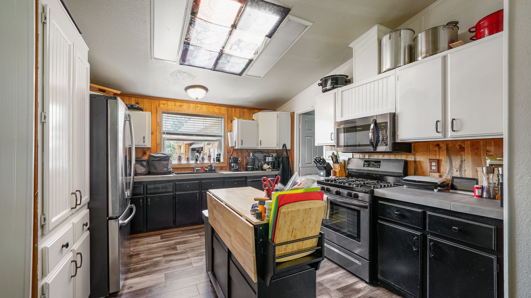 Kitchen featuring wood-finish flooring, a central island with a butcher block top, black cabinetry, concrete-finish countertops, and a stainless steel oven/range and microwave