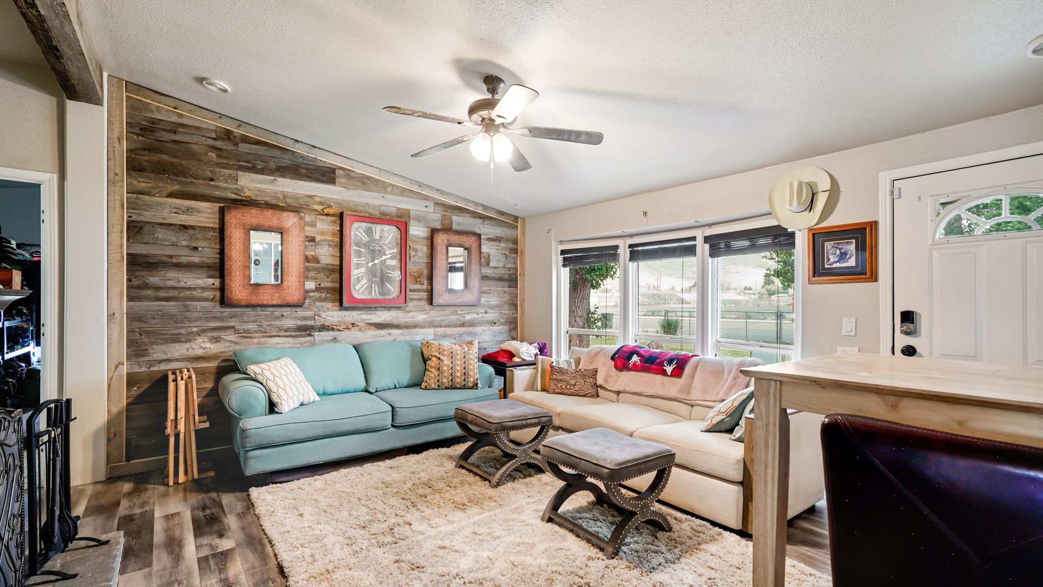 Living area featuring a distinctive wood plank accent wall, wood-finish flooring, and a ceiling fan