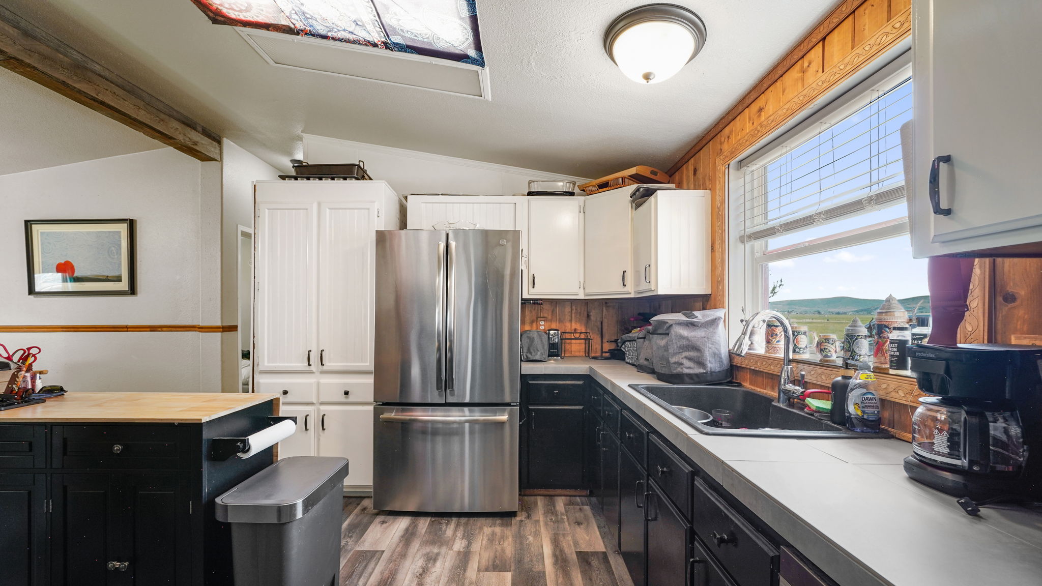 Kitchen featuring stainless steel refrigerator, white upper cabinetry, dark lower cabinetry, light countertops, and wood-finish flooring