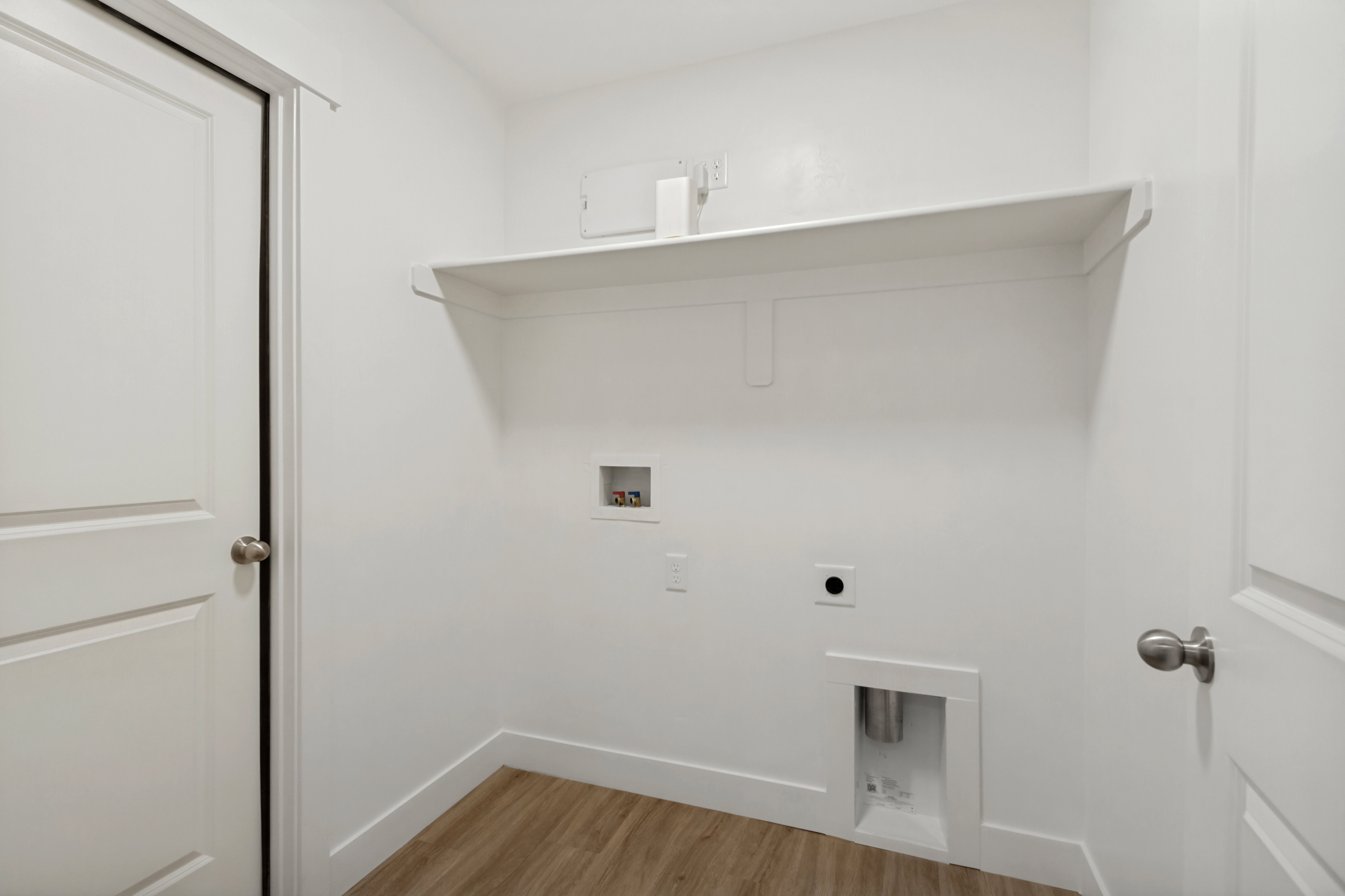 Utility area featuring a built-in shelf, wood-finish flooring, and white baseboards