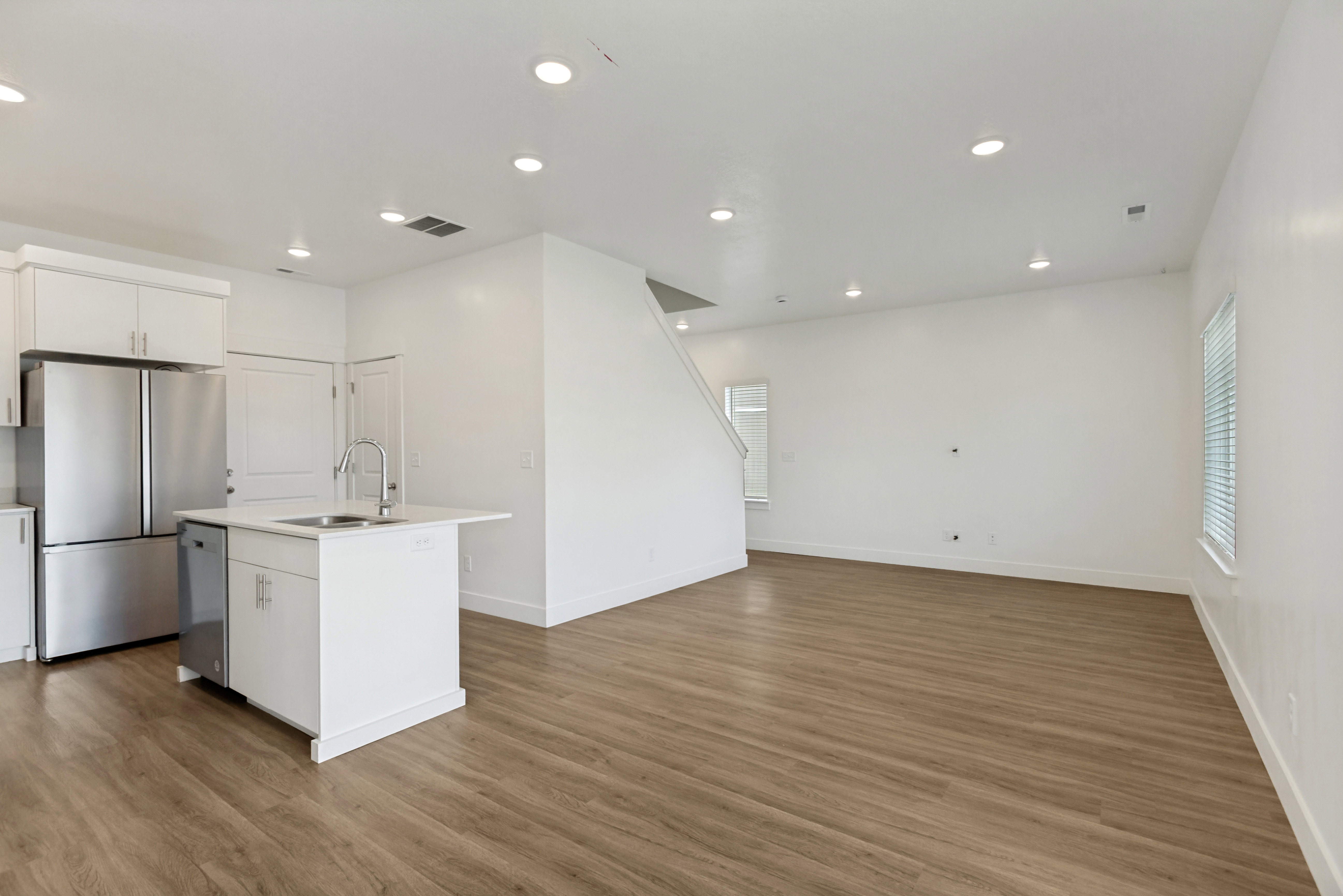 Open-concept living area featuring wood-finish flooring, white walls, recessed lighting, and a quartz kitchen island