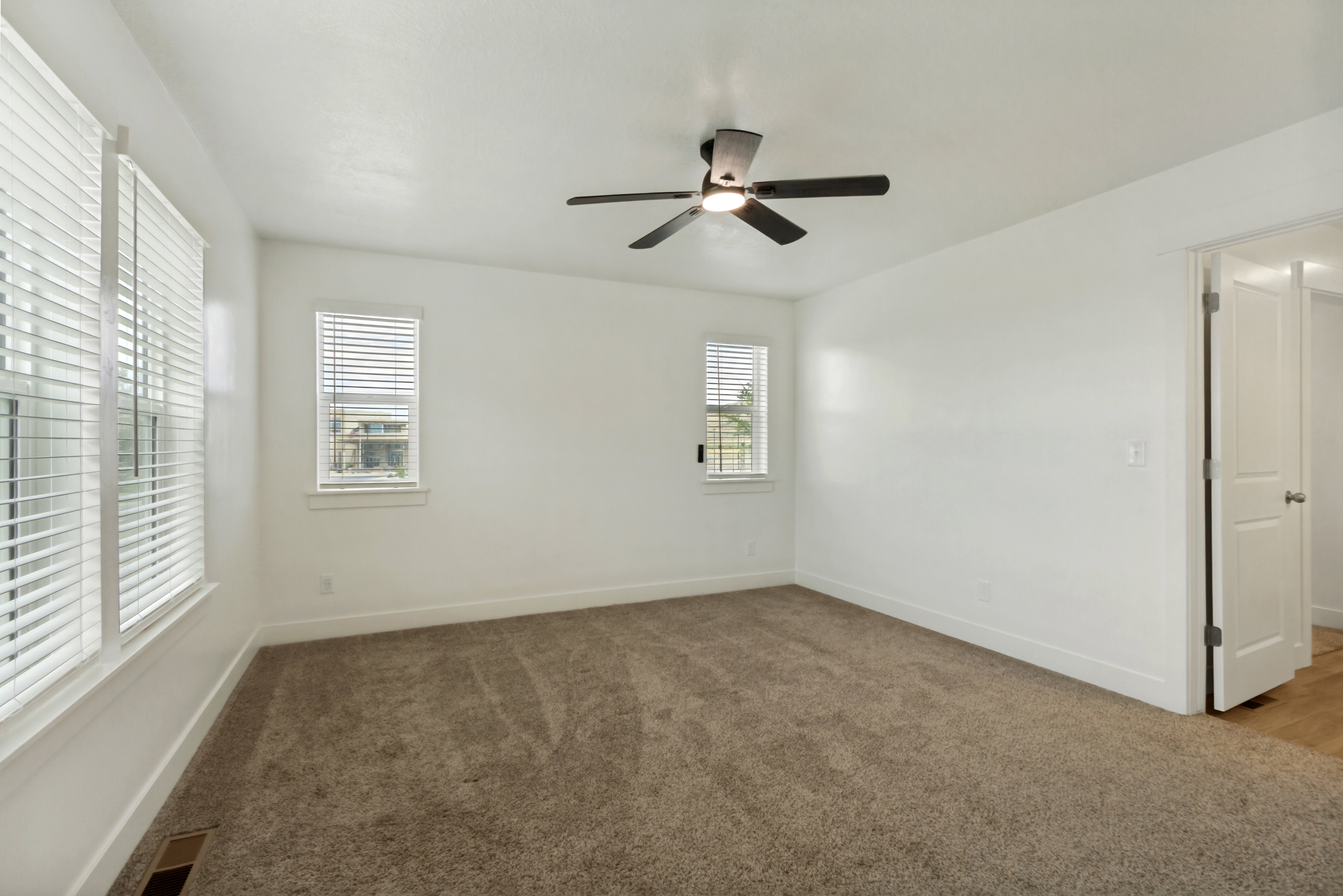 Spacious master suite featuring multiple windows, a ceiling fan with integrated lighting, and a white paneled door