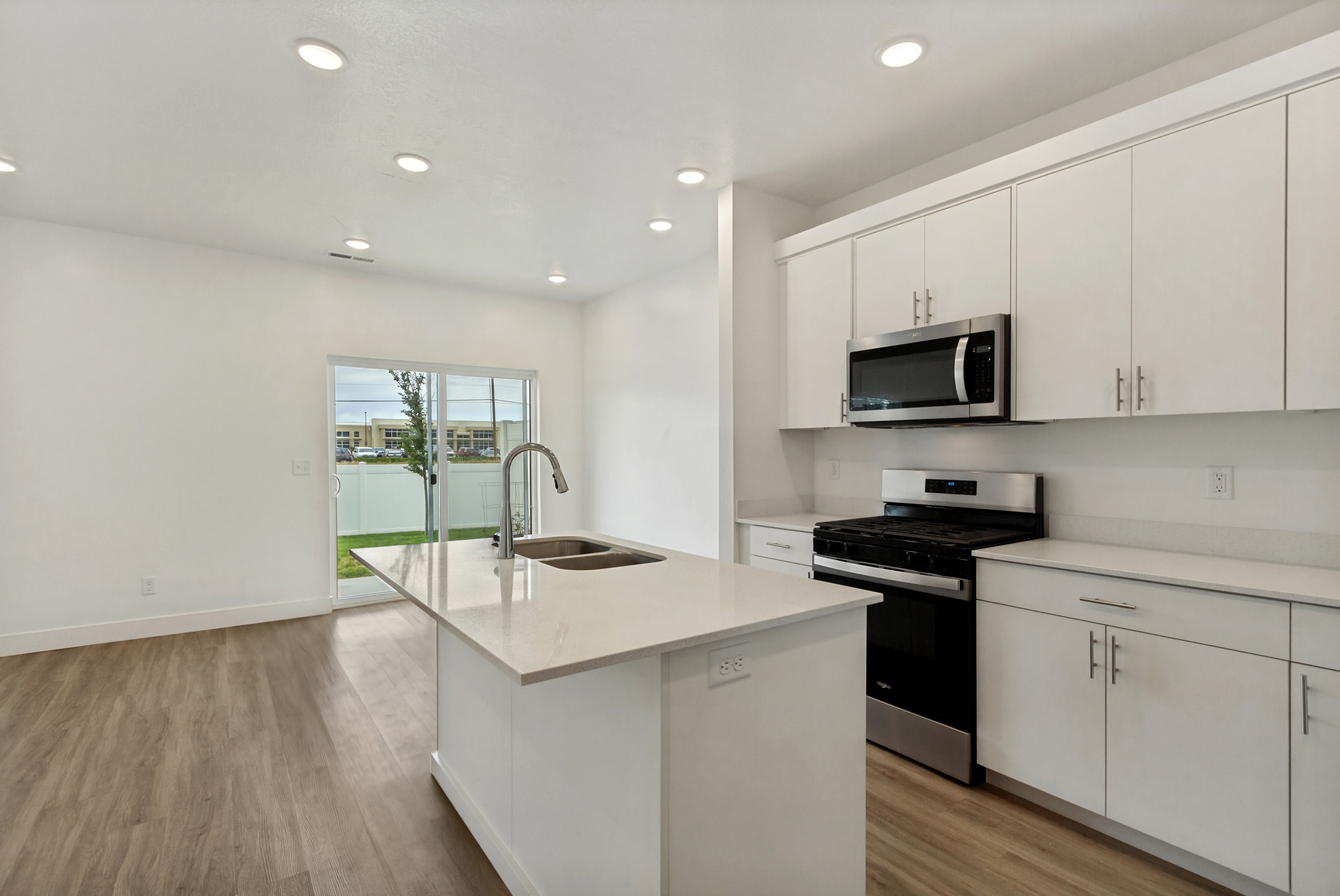 Modern kitchen featuring an quartz island with a double basin sink, white cabinetry, integrated stainless steel microwave, gas range, and laminate flooring