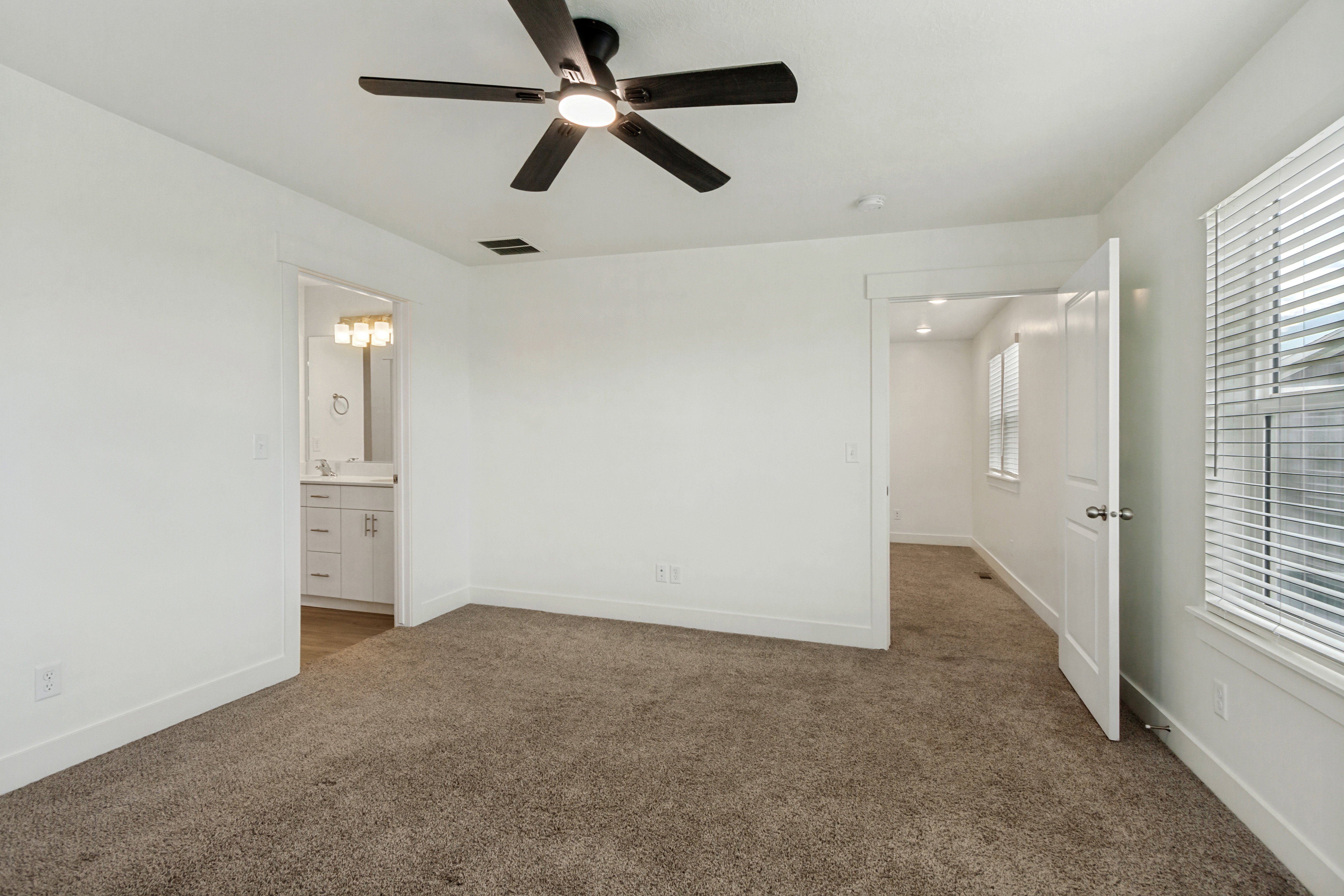 Spacious master suite featuring multiple windows, a ceiling fan with integrated lighting, and a white paneled door