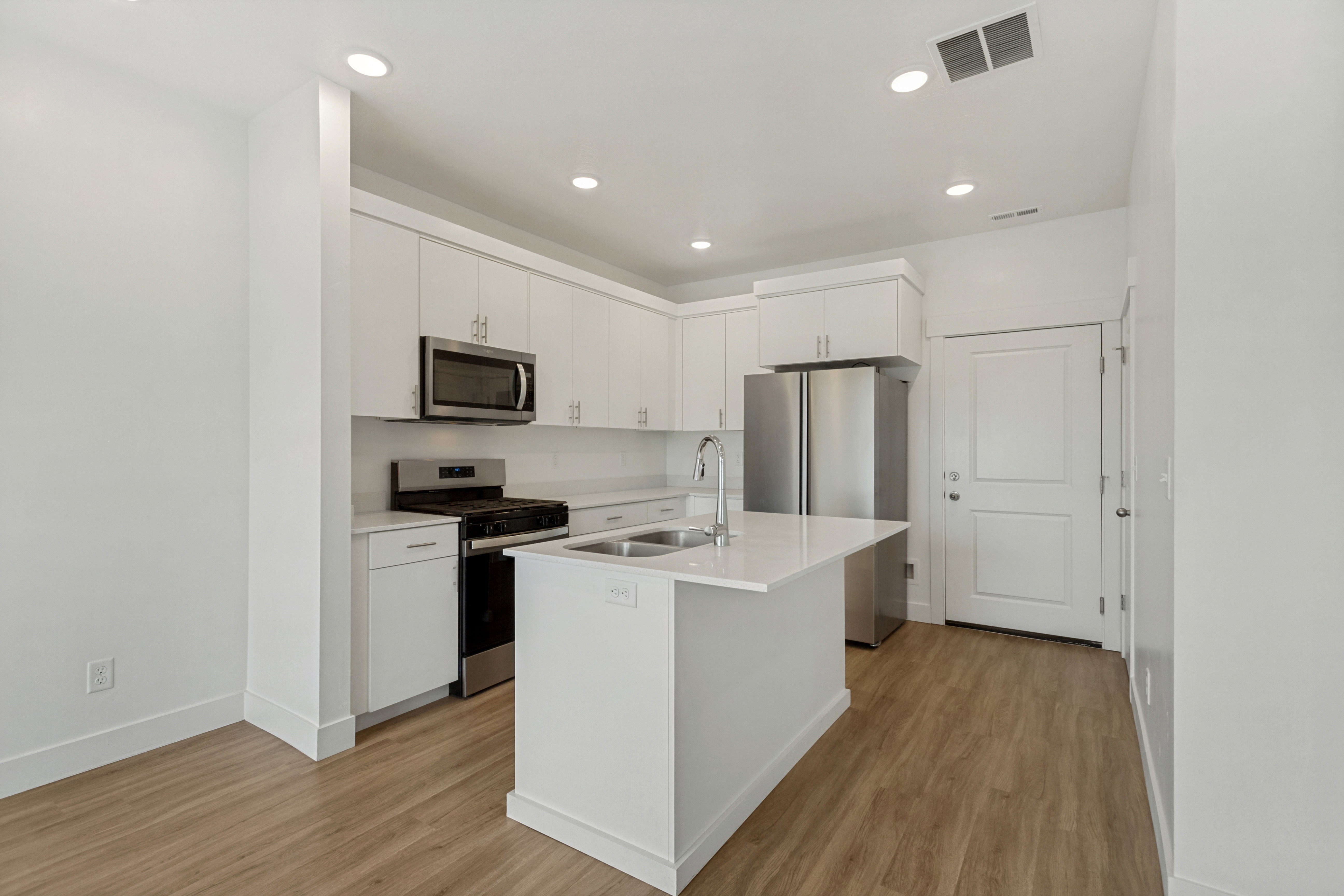Modern kitchen featuring an quartz island with a double basin sink, white cabinetry, integrated stainless steel microwave, gas range, and laminate flooring