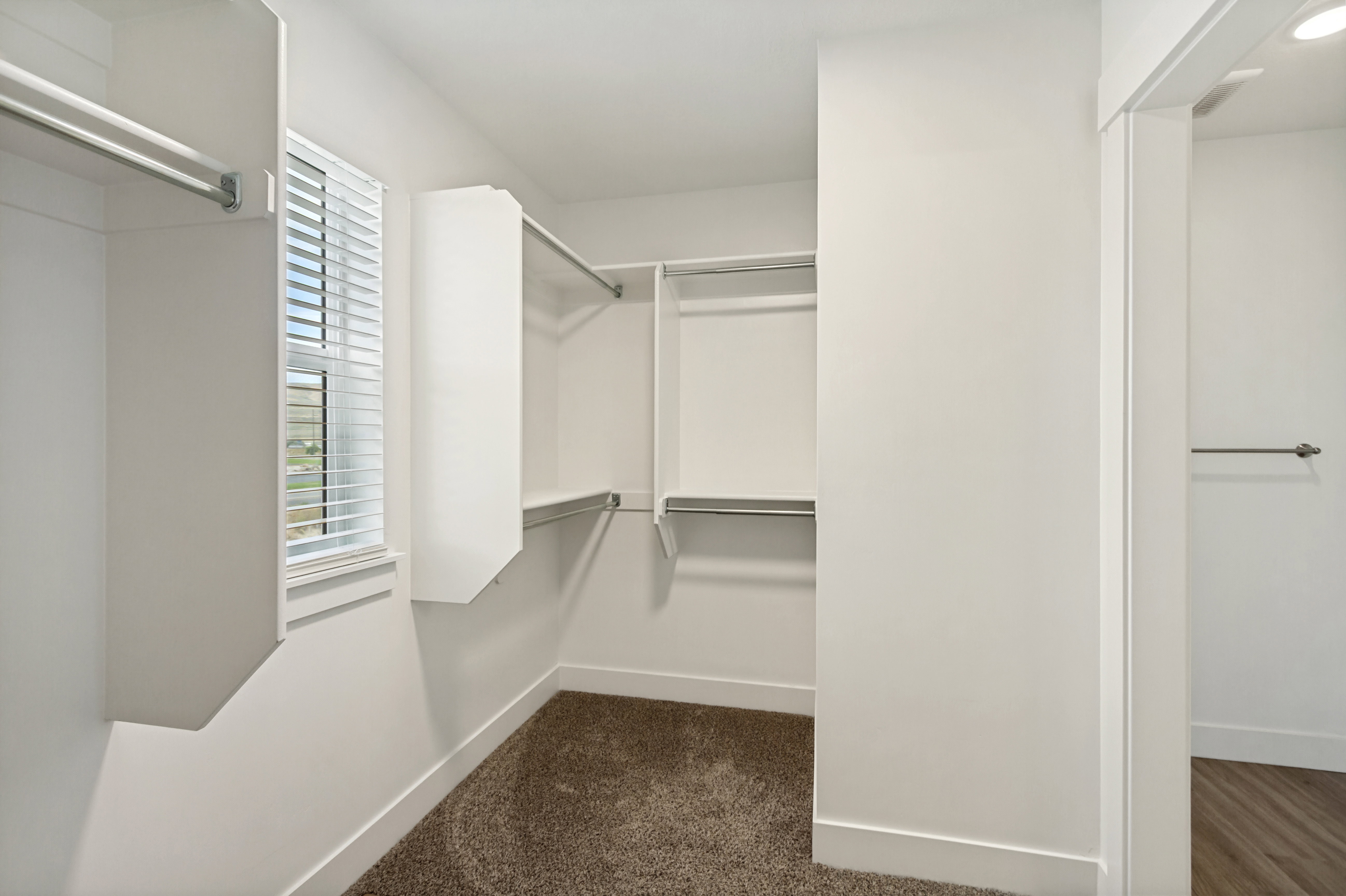 Walk-in closet featuring white built-in shelving, hanging rods, and a window with blinds