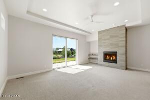 Spacious room featuring a stone-clad fireplace, built-in shelving, tray ceiling, recessed lighting, and sliding glass doors opening to outdoor green space