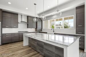 Gourmet kitchen featuring a large central island with a stone countertop, dark wood-finish cabinetry, stainless steel appliances, pendant lighting, and wood-finish flooring